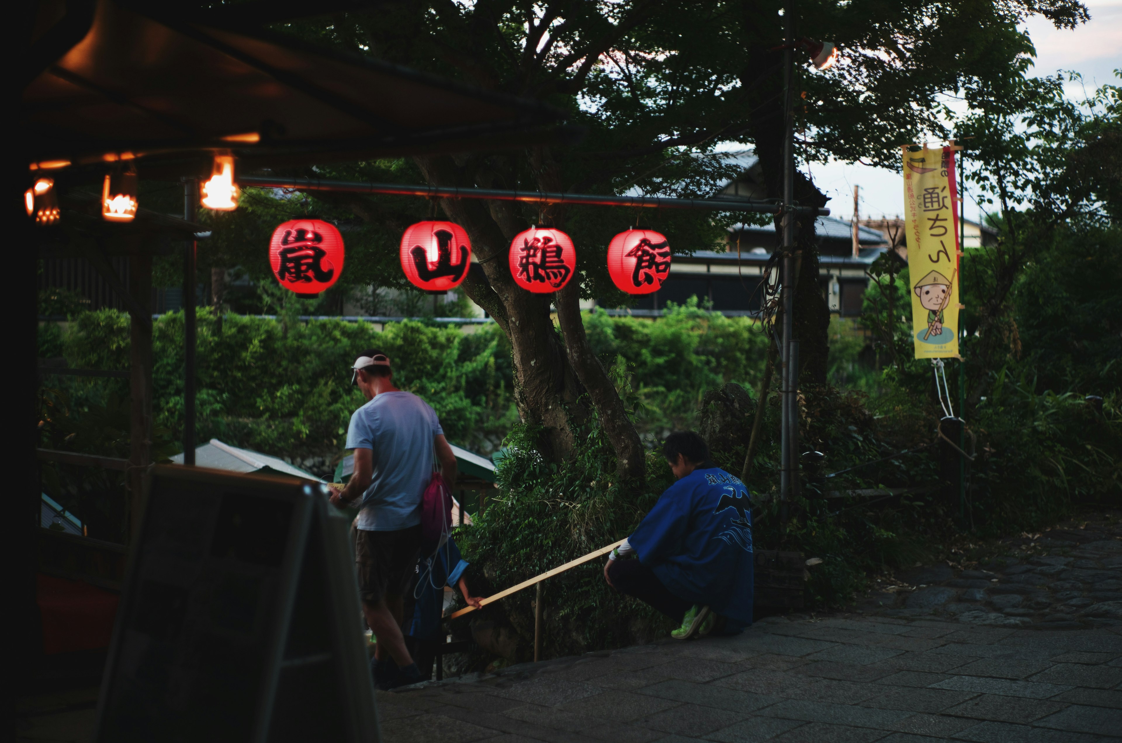 Outdoor market at dusk with hanging lanterns and people working