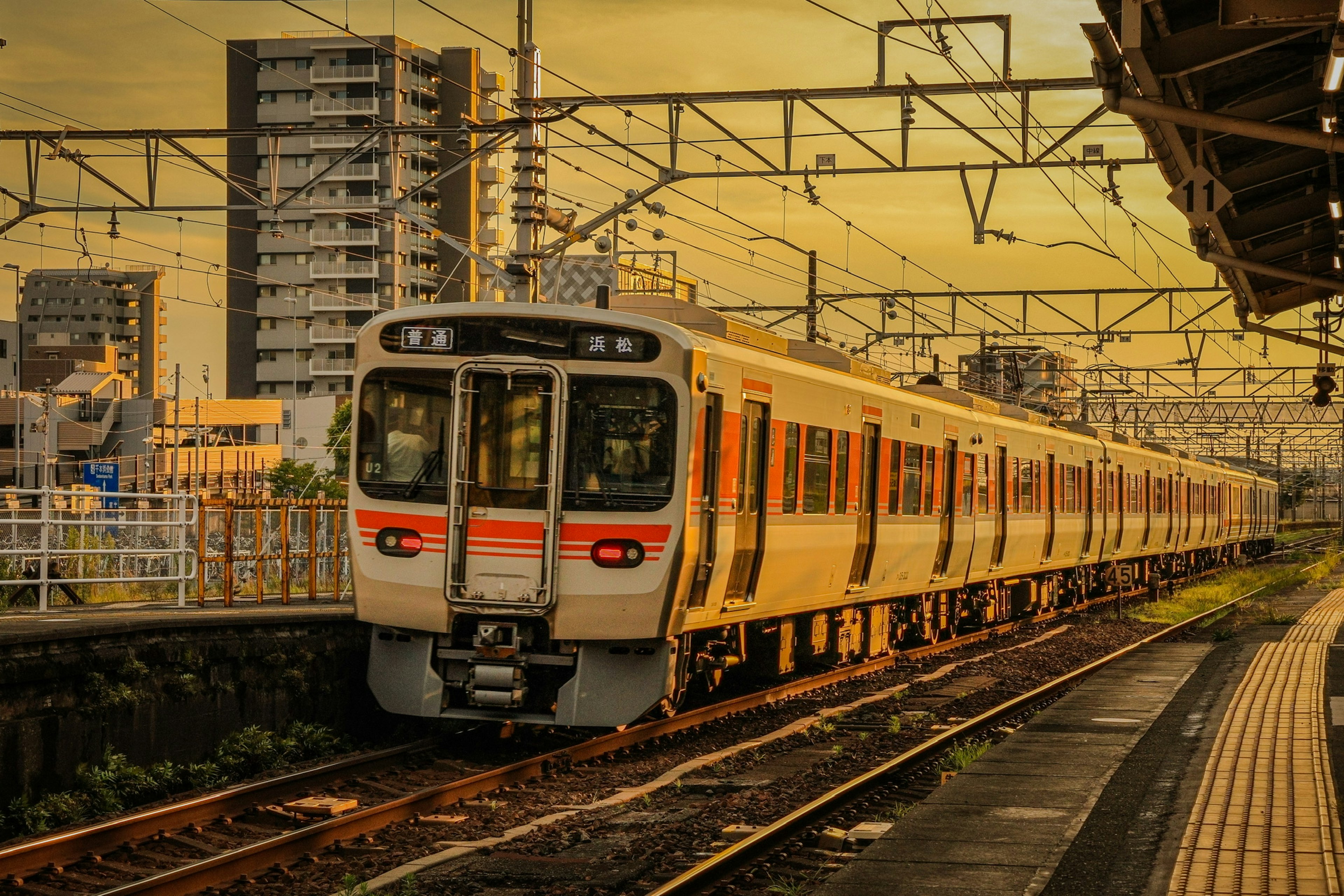 Train stopped at a station during sunset with surrounding buildings