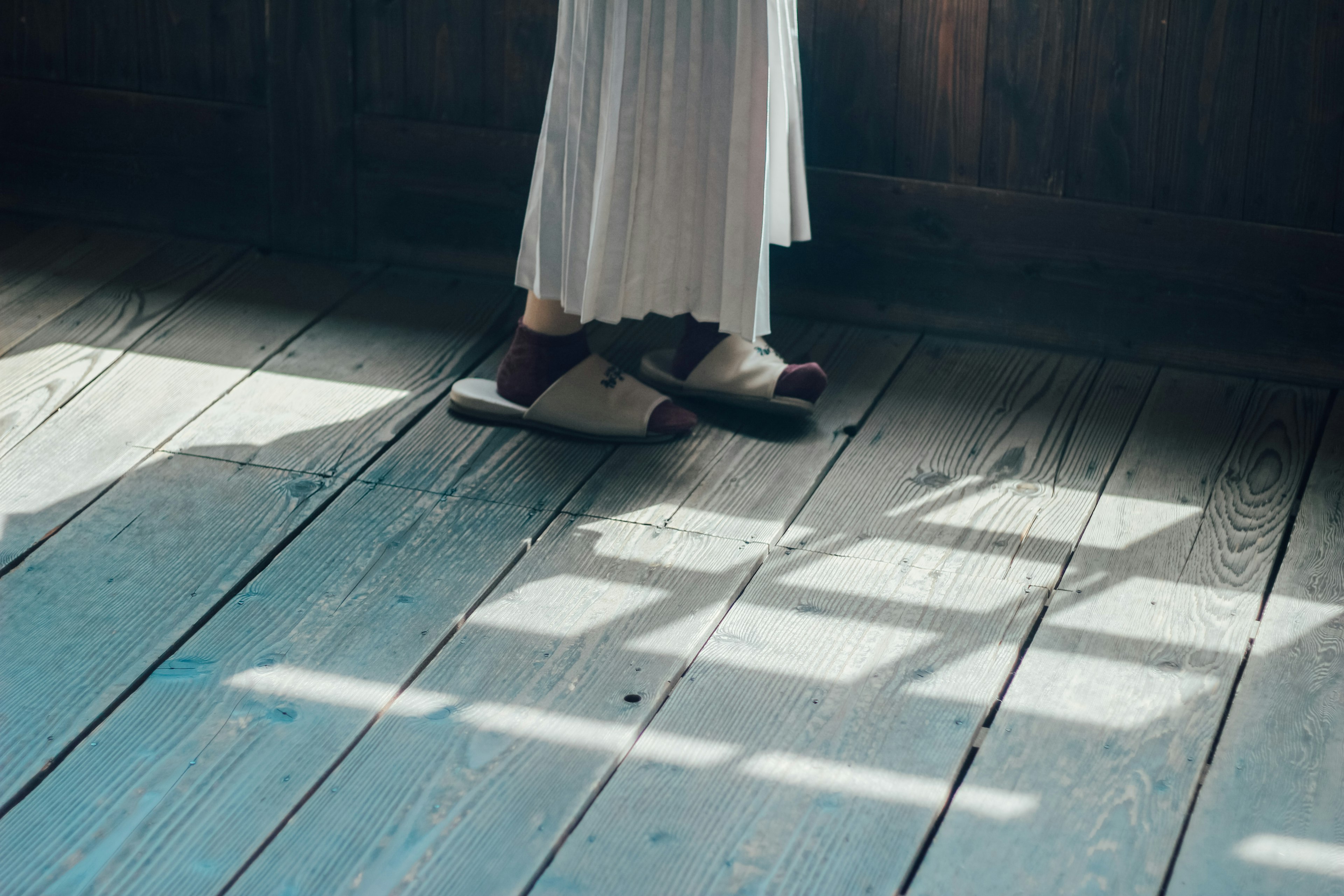 A person's feet in a light white dress standing on a wooden floor