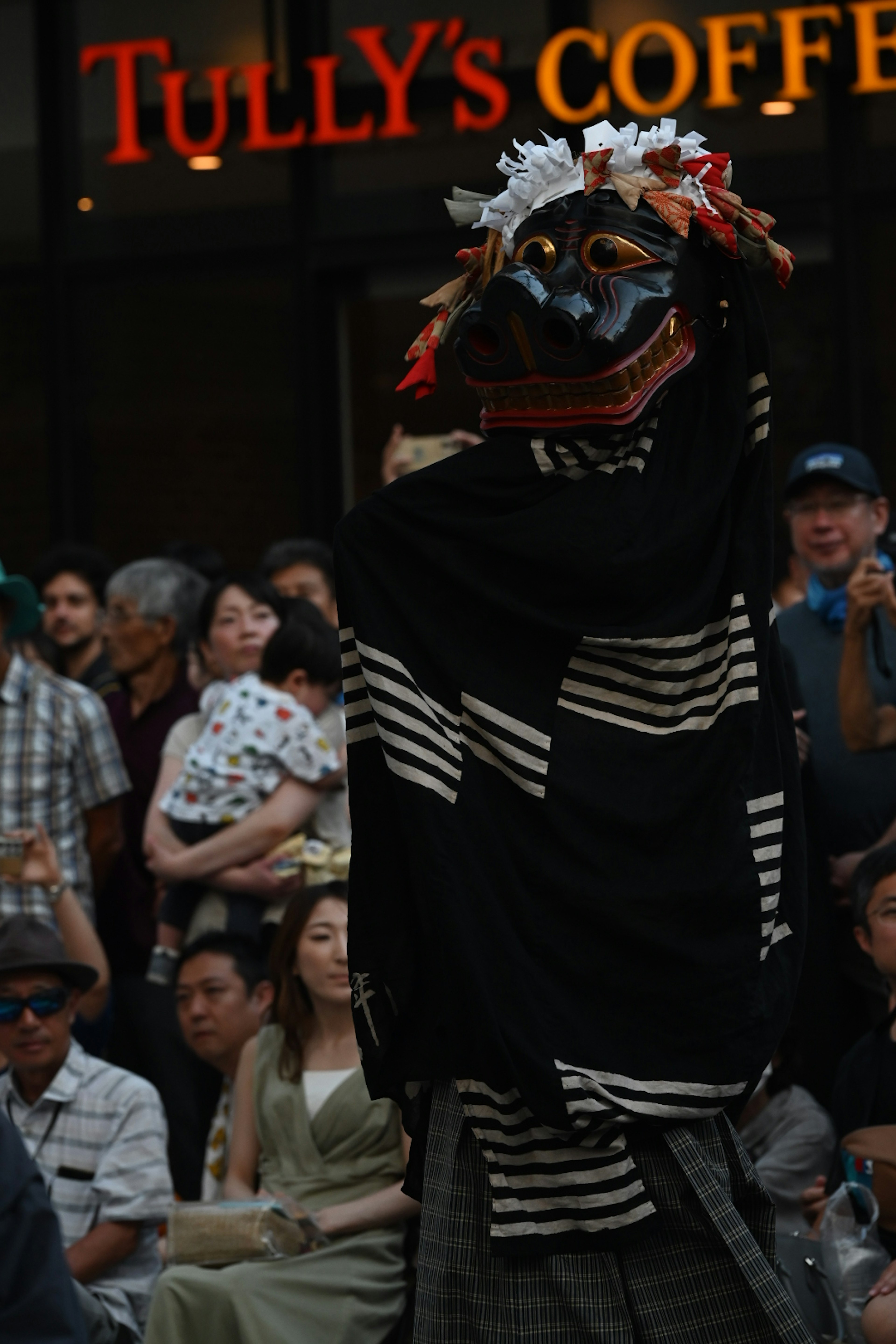 A person in traditional attire performing with a decorative headpiece in front of a Tully's Coffee sign