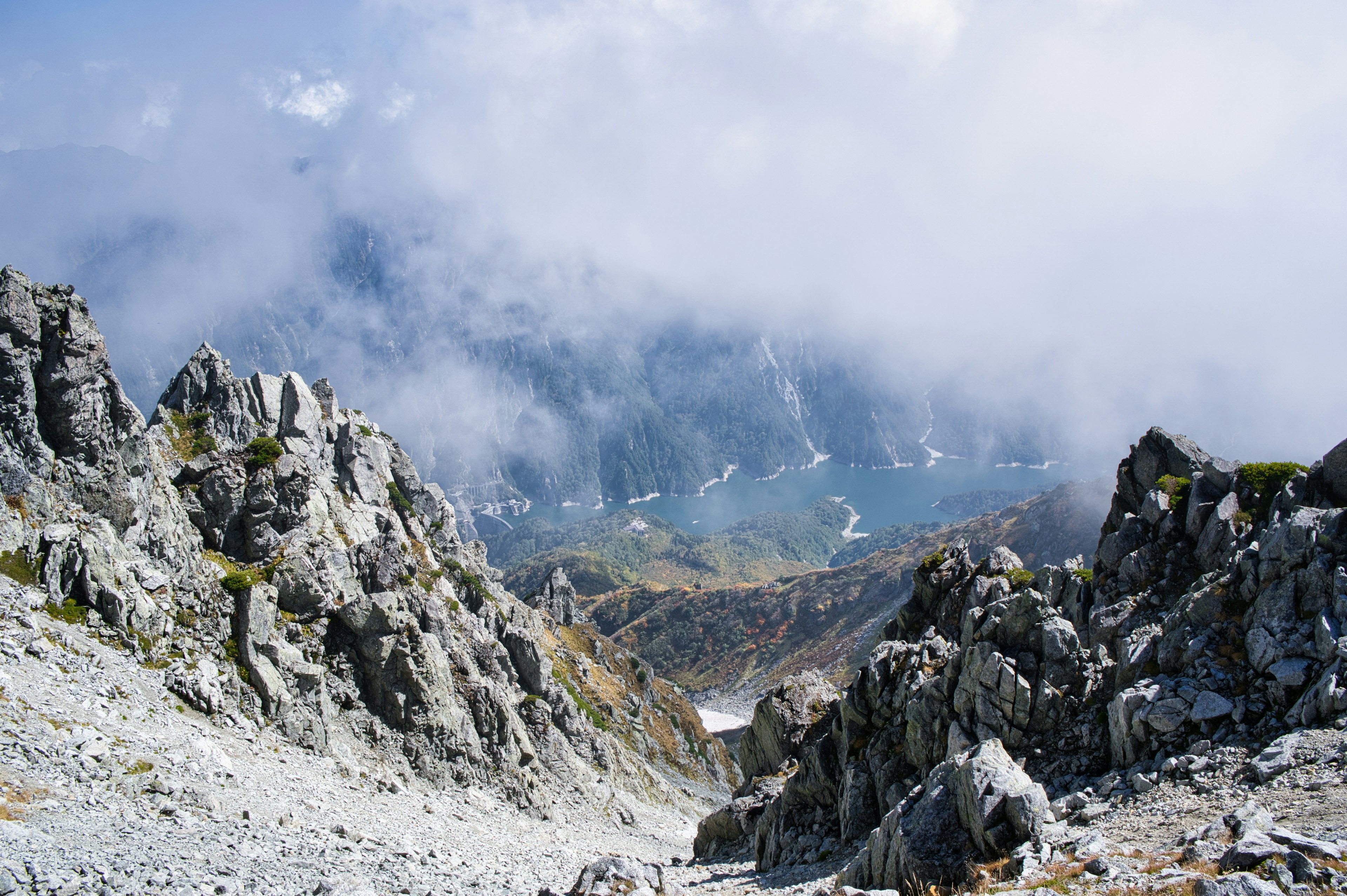 A valley view shrouded in mist featuring rocky cliffs and a glimpse of a blue lake