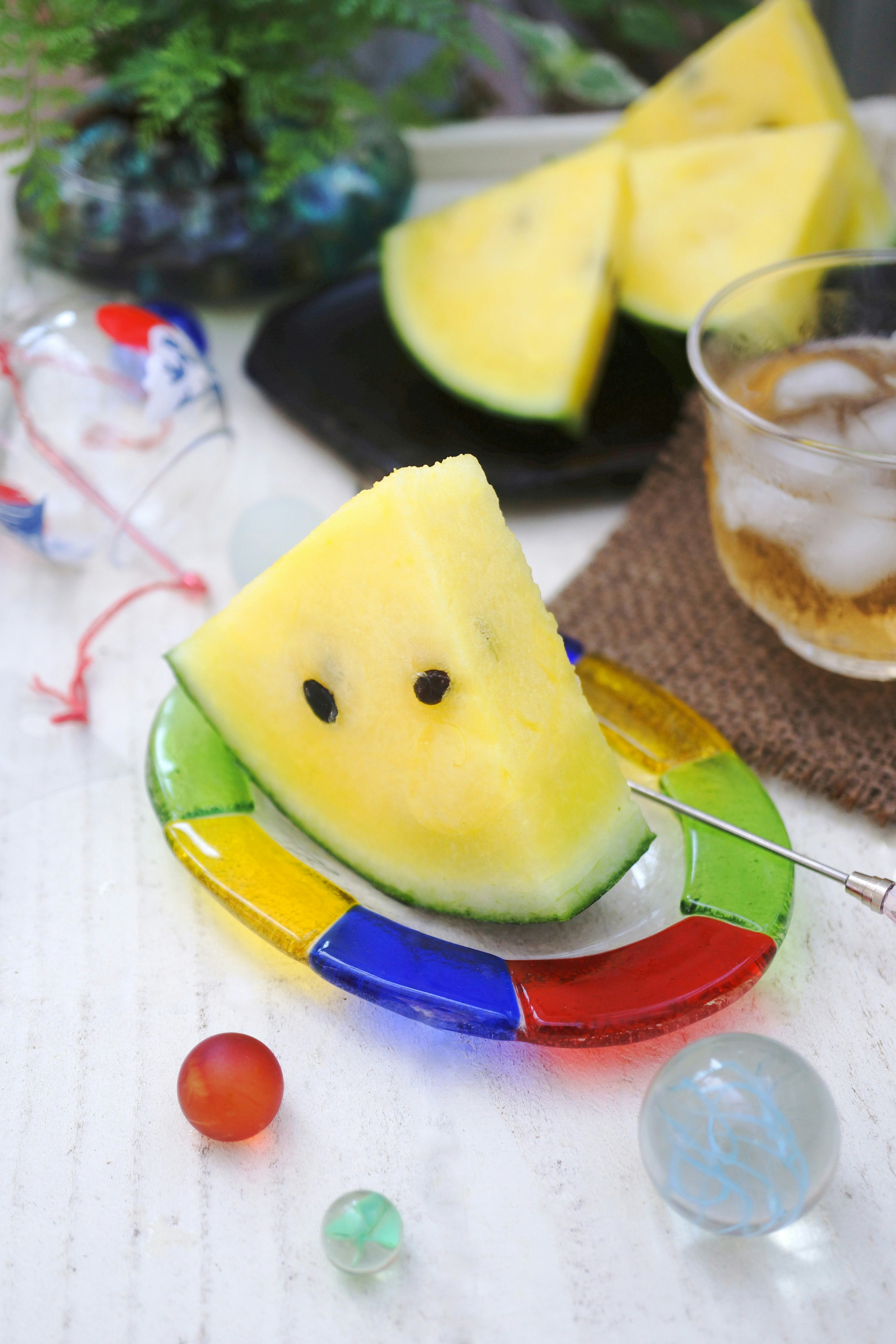 Slice of watermelon shaped like a smile on a colorful plate with a drink and decorative marbles