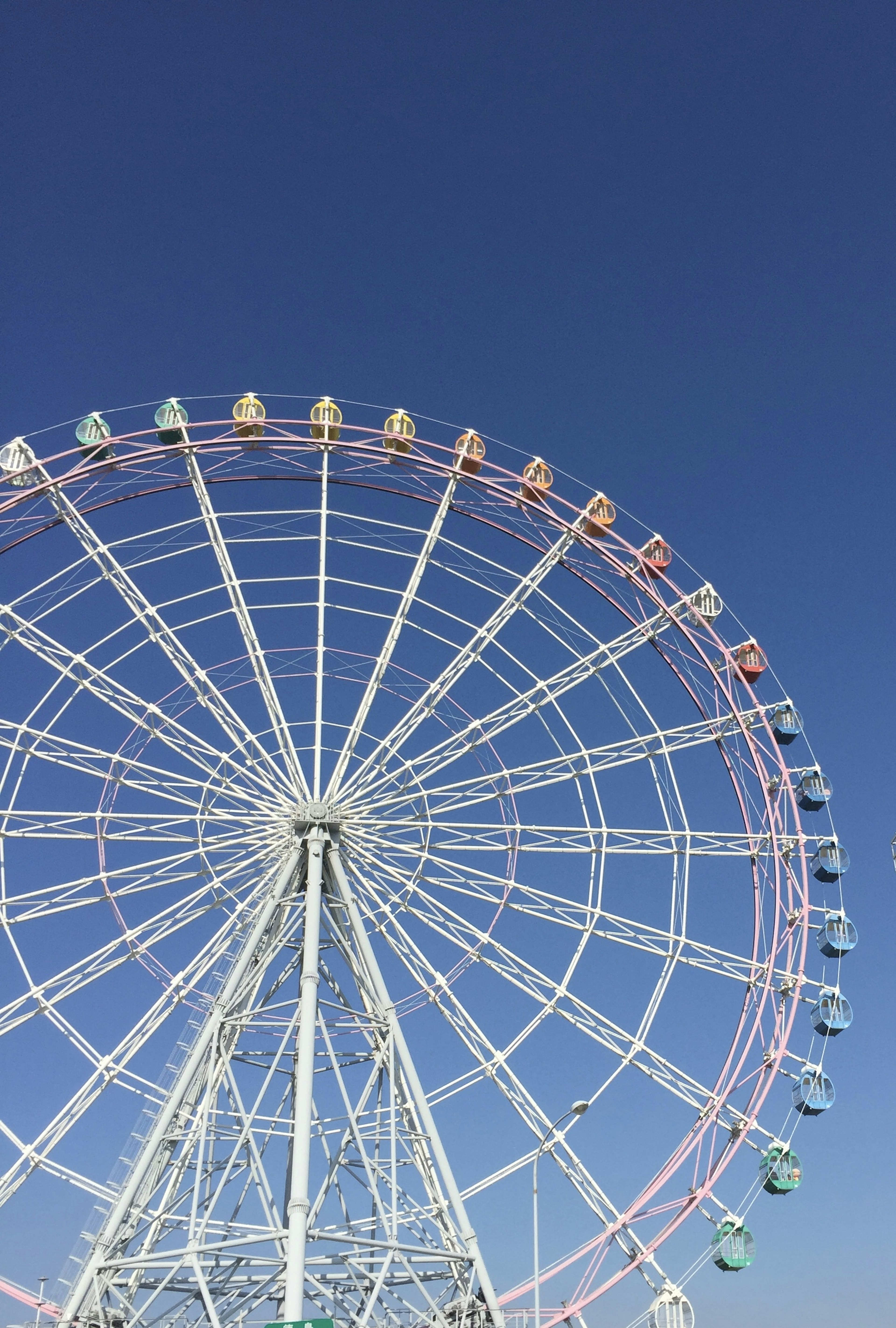 Seitenansicht eines großen Riesenrads unter einem blauen Himmel farbenfrohe Kapseln angeordnet