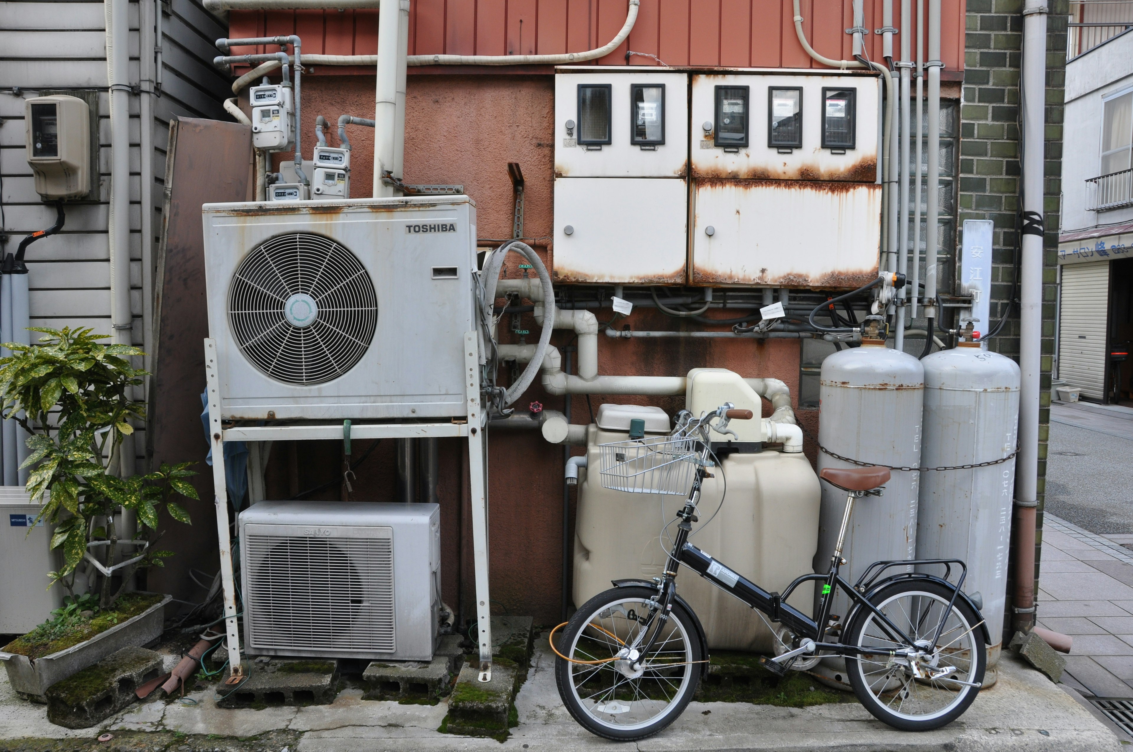 古い建物の裏側にあるエアコンとガスボンベと小さな自転車