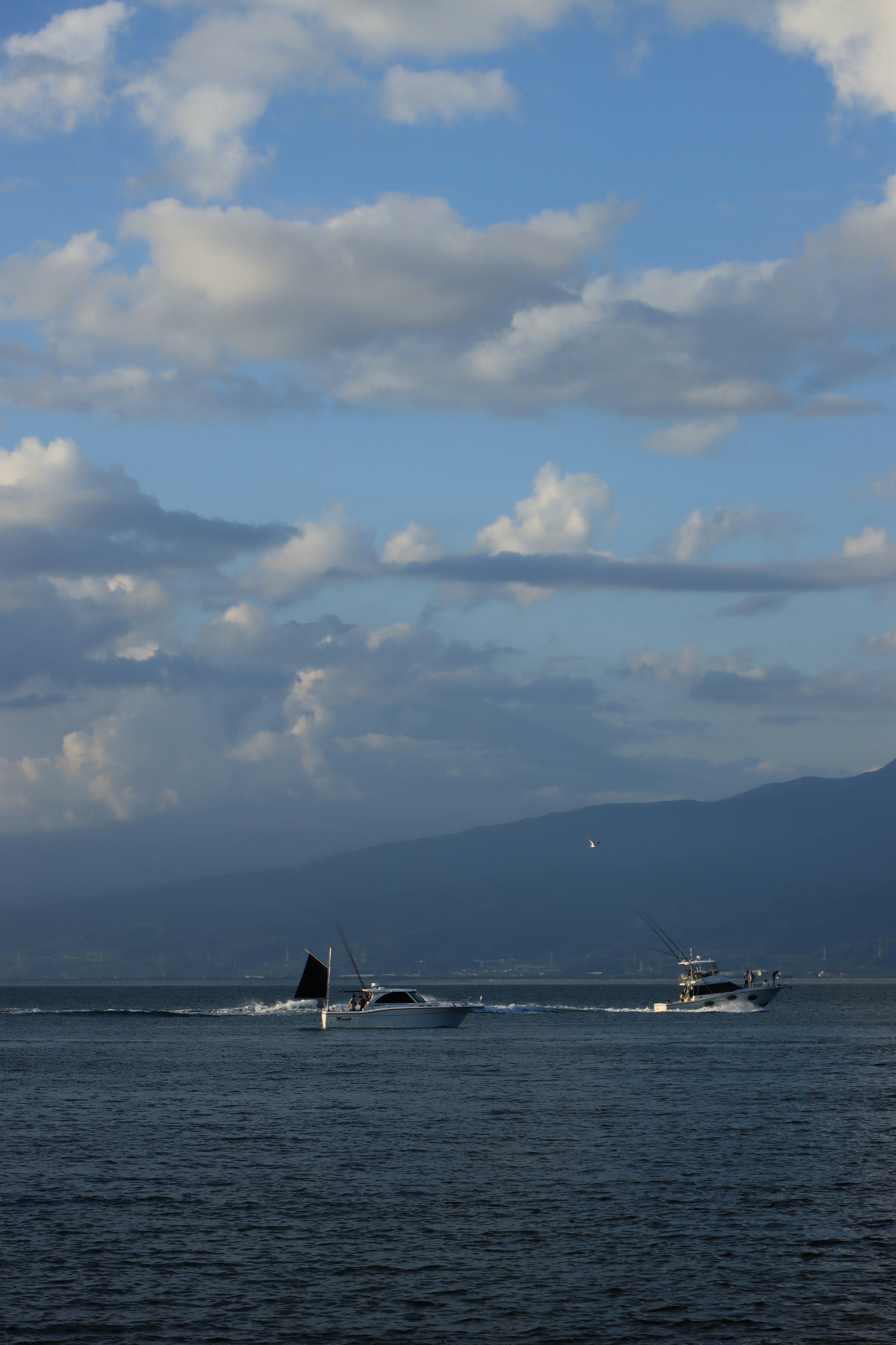 Multiple boats navigating on a blue sea under a cloudy sky