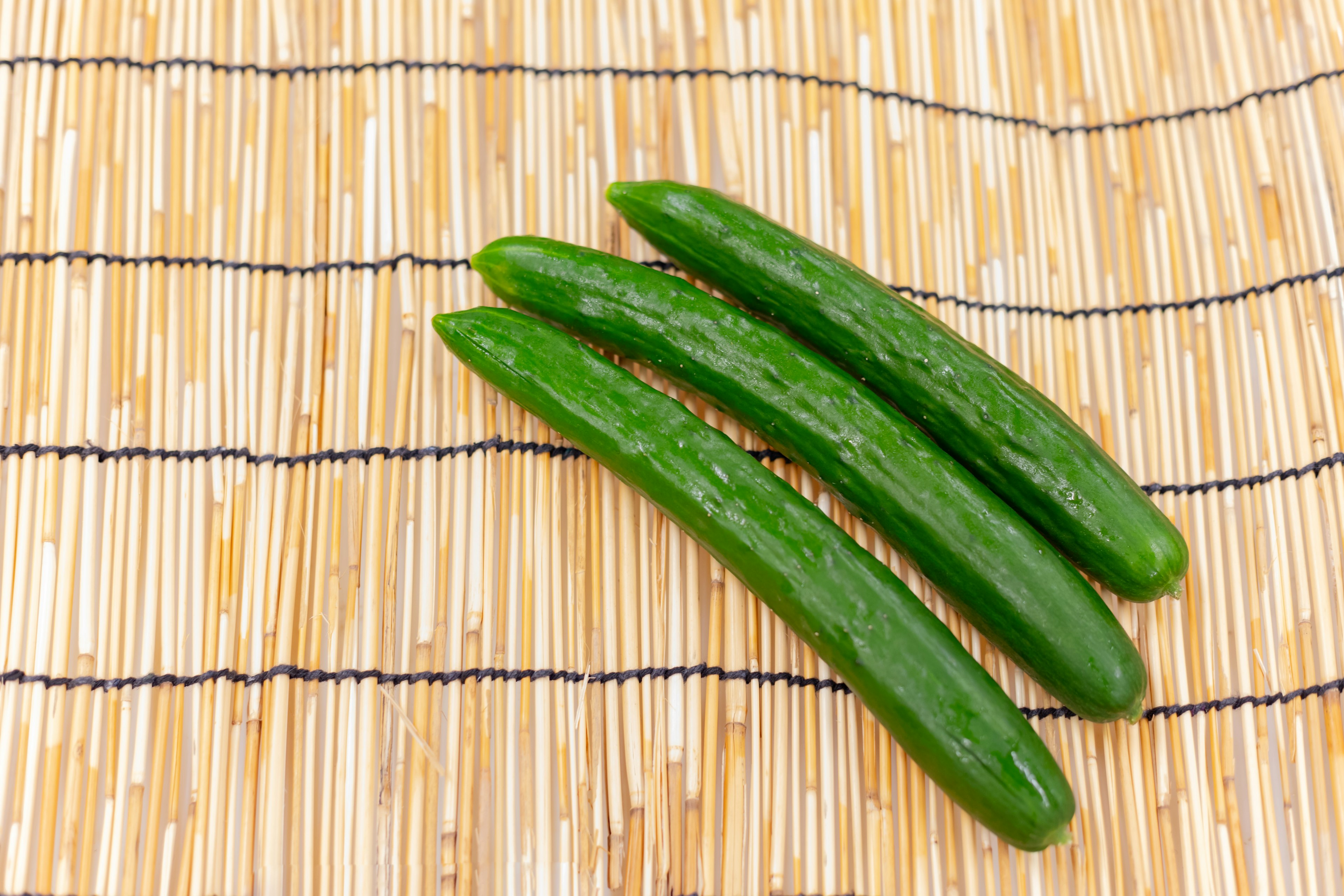 Three fresh cucumbers placed on a bamboo mat