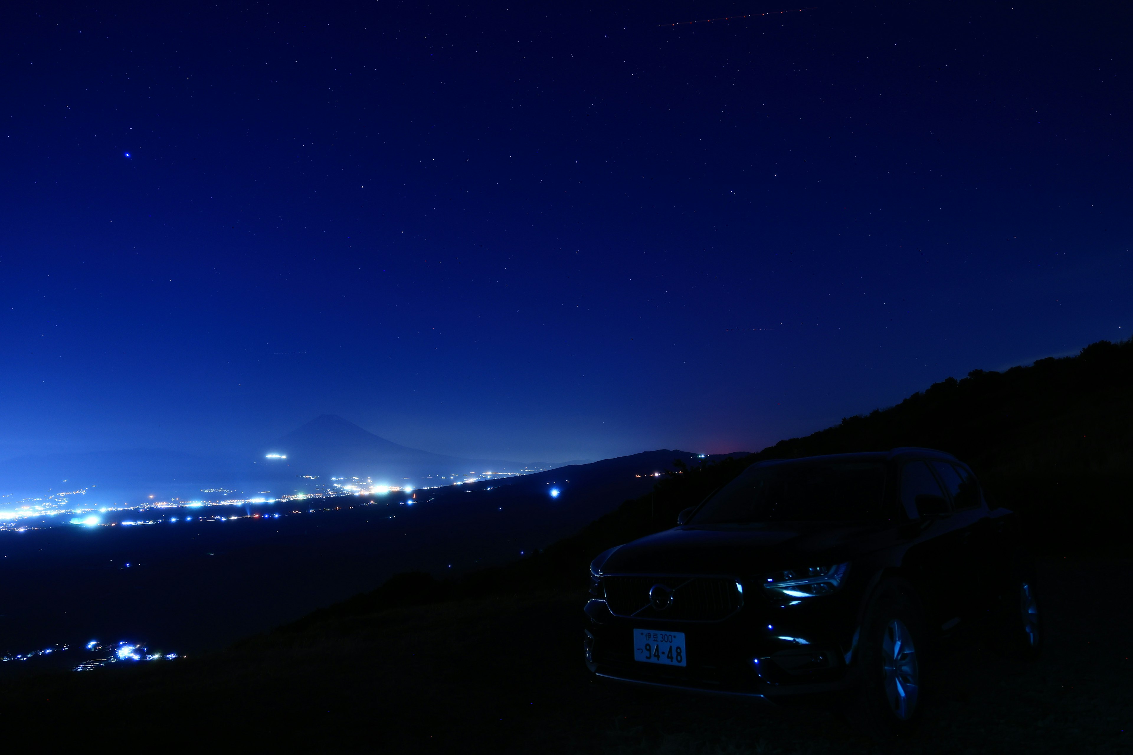 Auto nera con luci della città e stelle nel cielo notturno