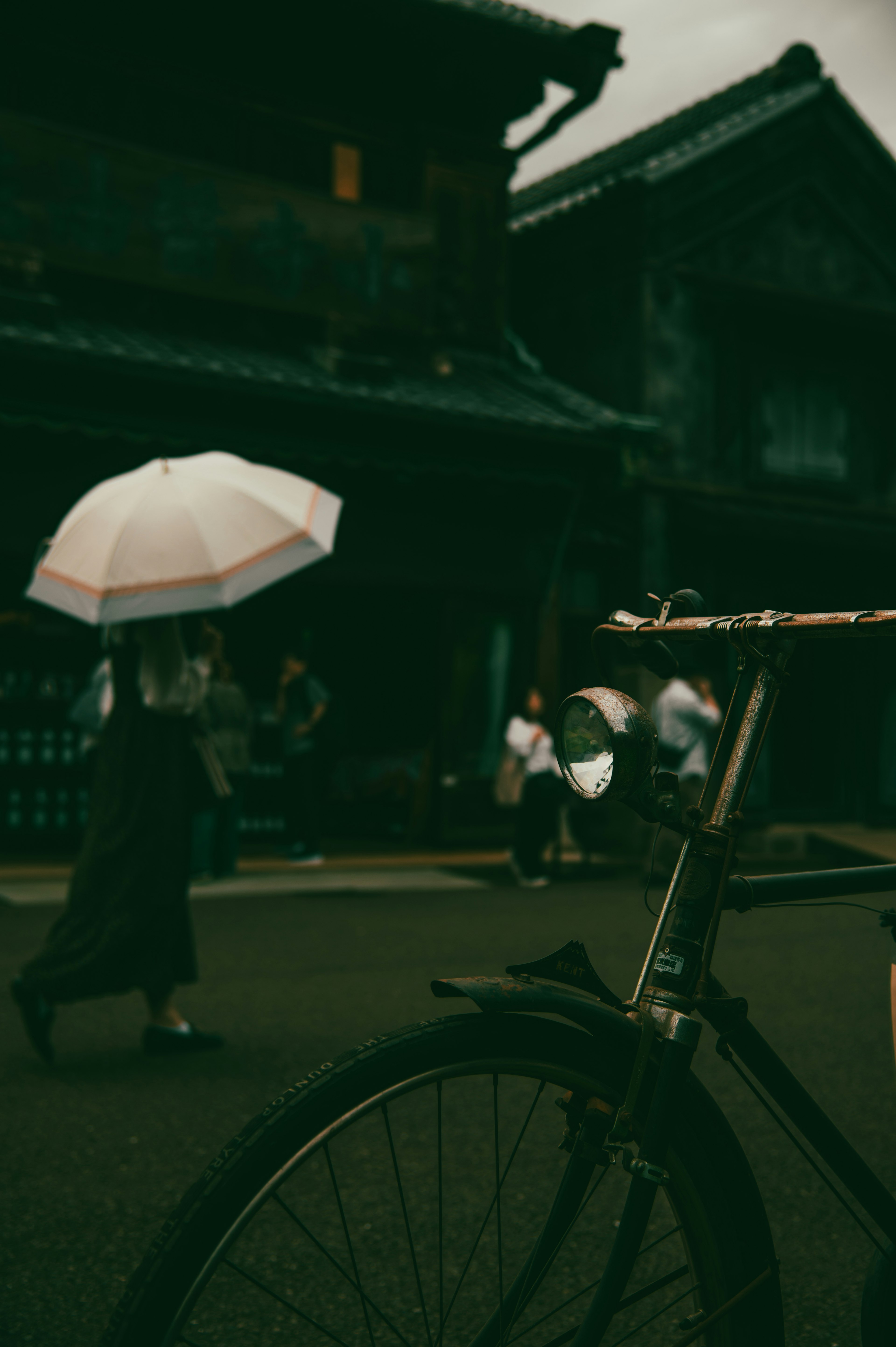 A person walking with an umbrella in the foreground of a bicycle old buildings in the background