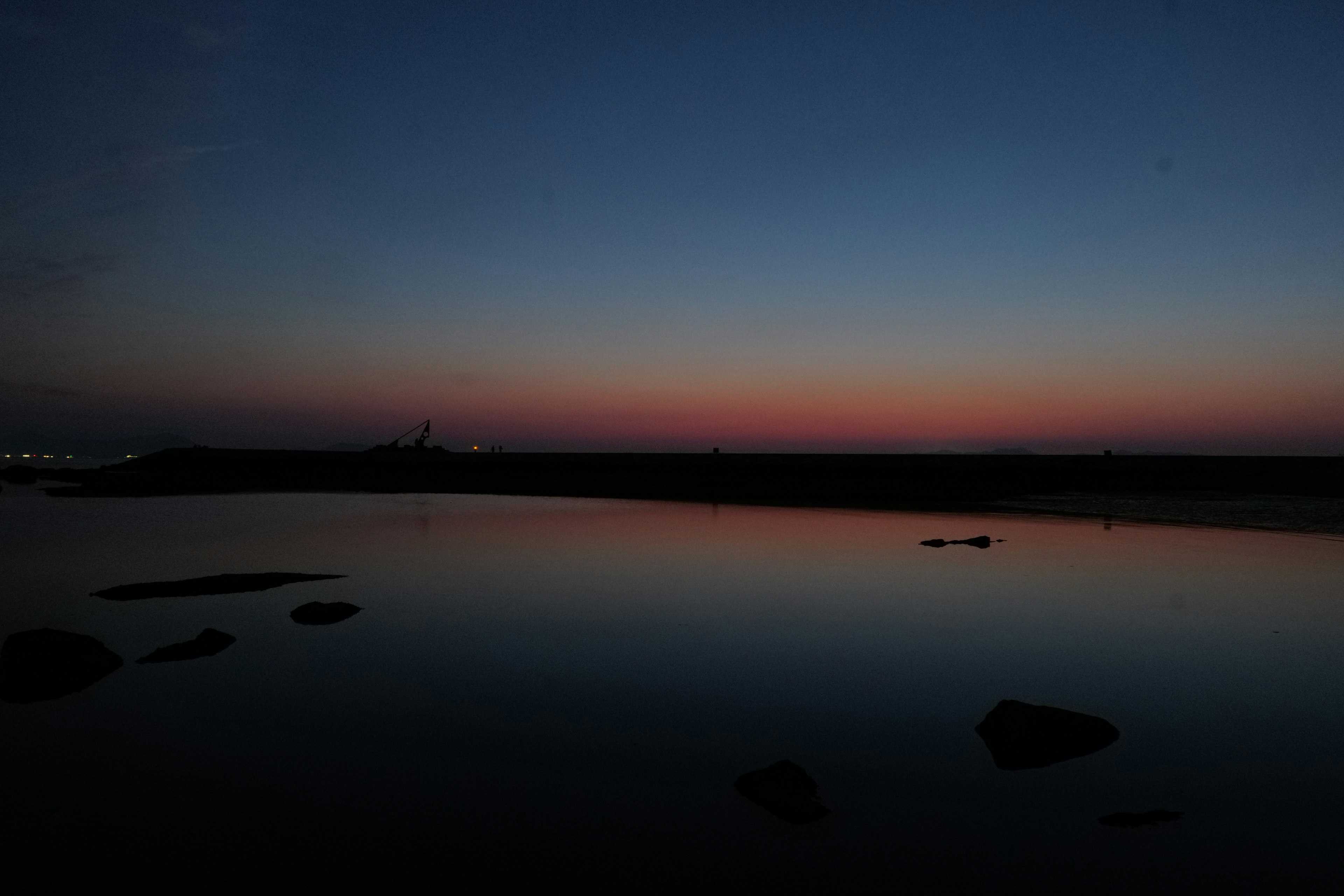 Ruhiges Wasser, das Morgendämmerungsfarben mit dunklem Horizont spiegelt