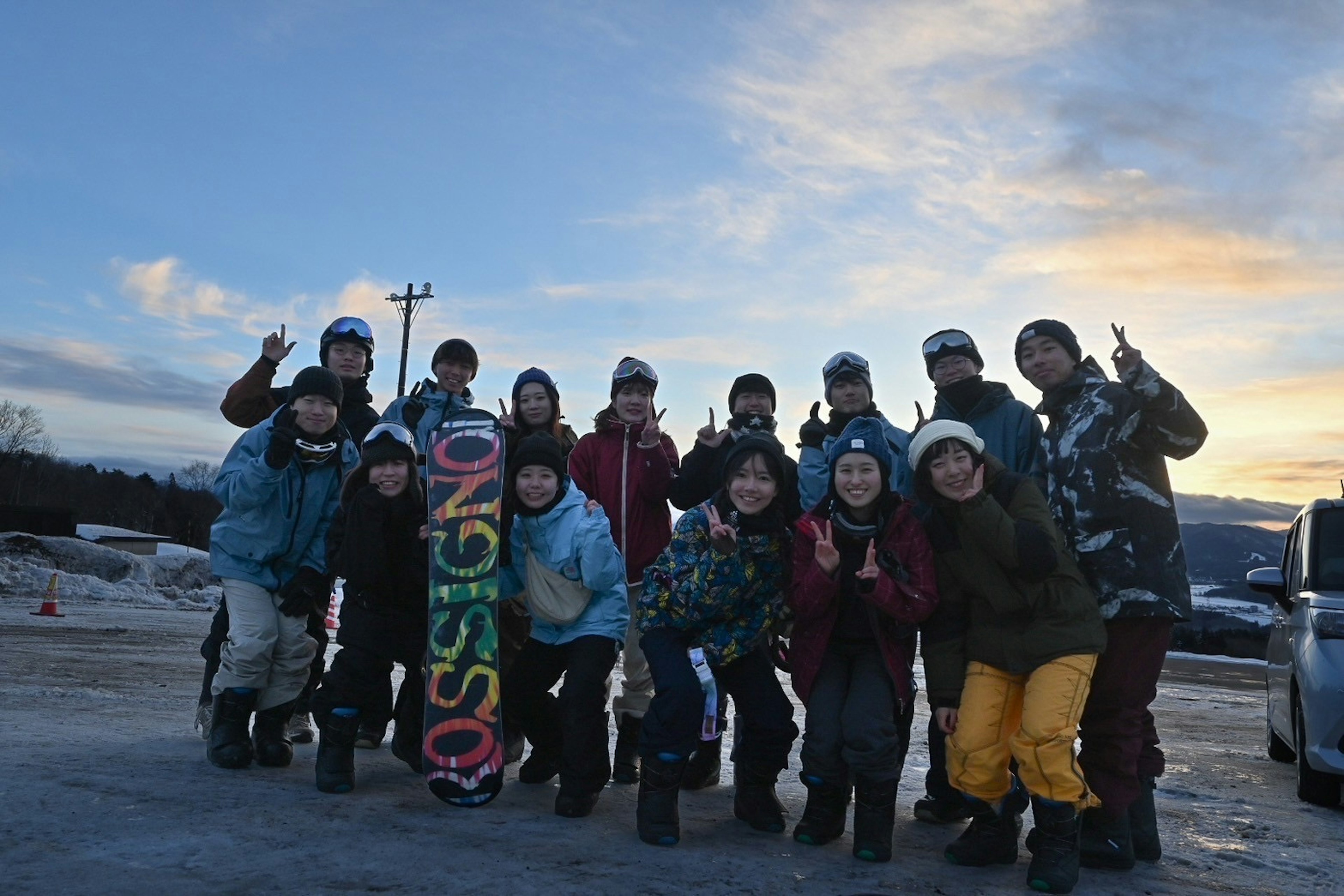 A group of young people posing with a snowboard during sunset