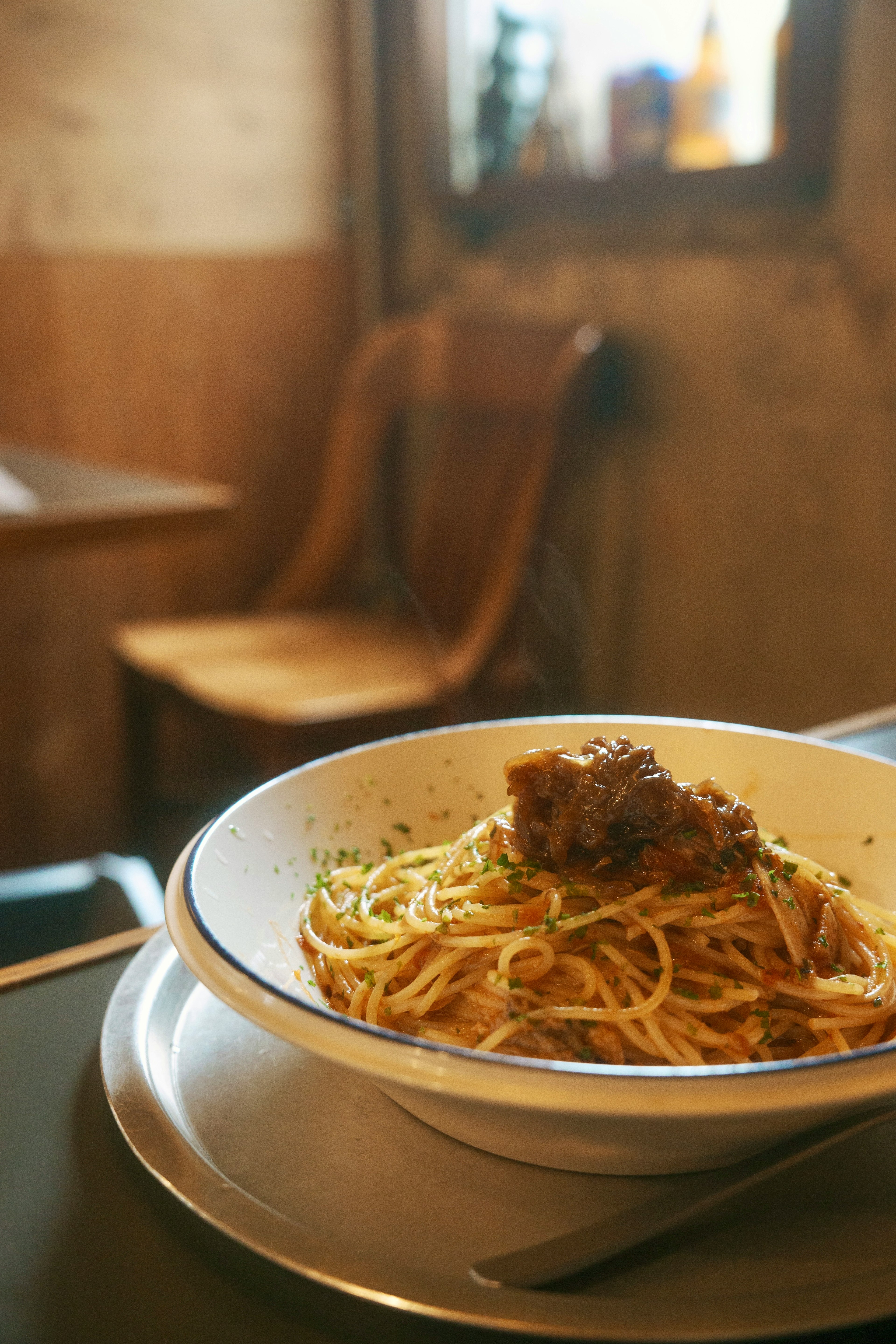 Una ciotola di spaghetti su un piatto con una sedia di legno in un caffè