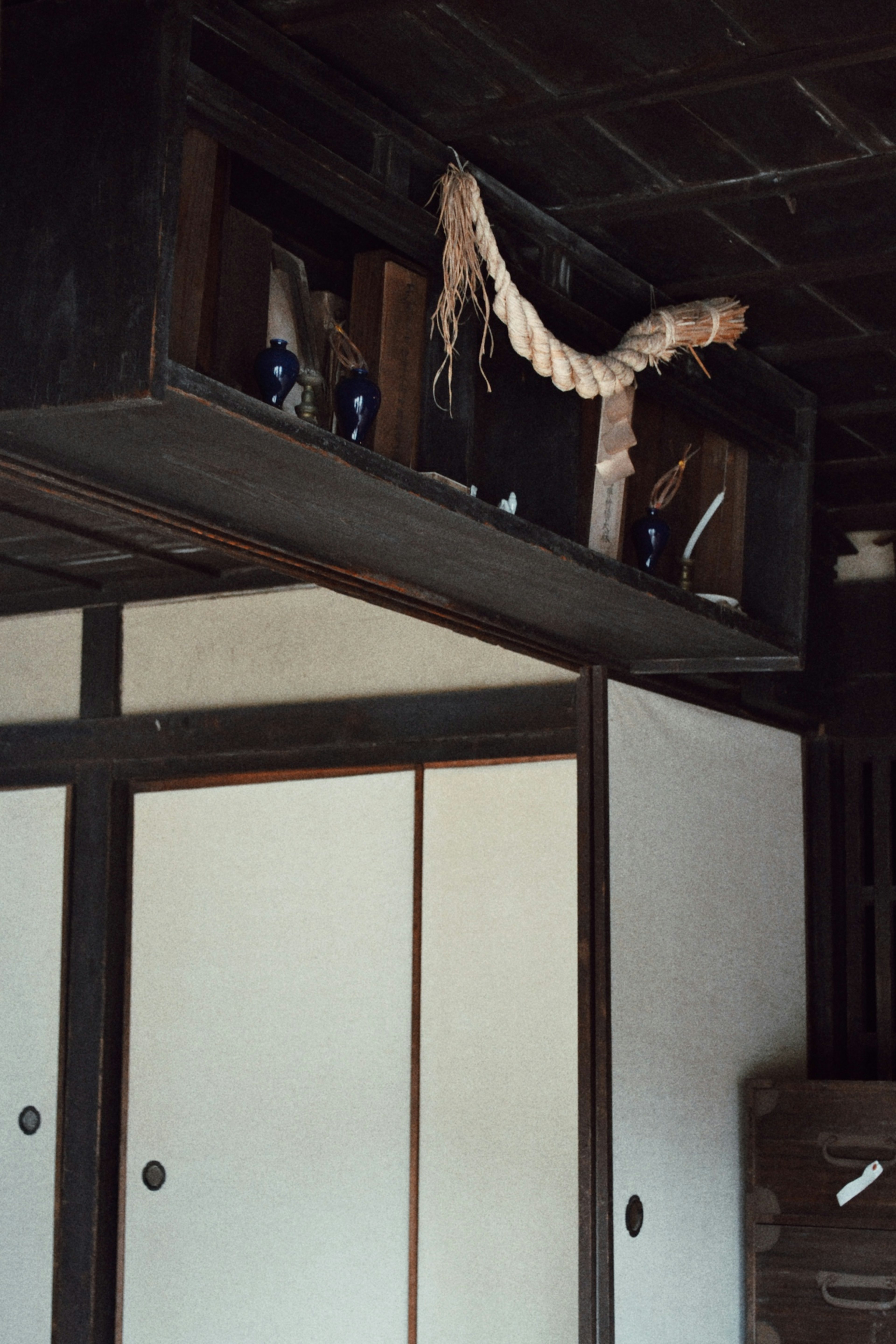 Innenansicht eines alten japanischen Hauses mit schwarzer Decke und weißen Schiebetüren mit blauen Flaschen auf einem Regal