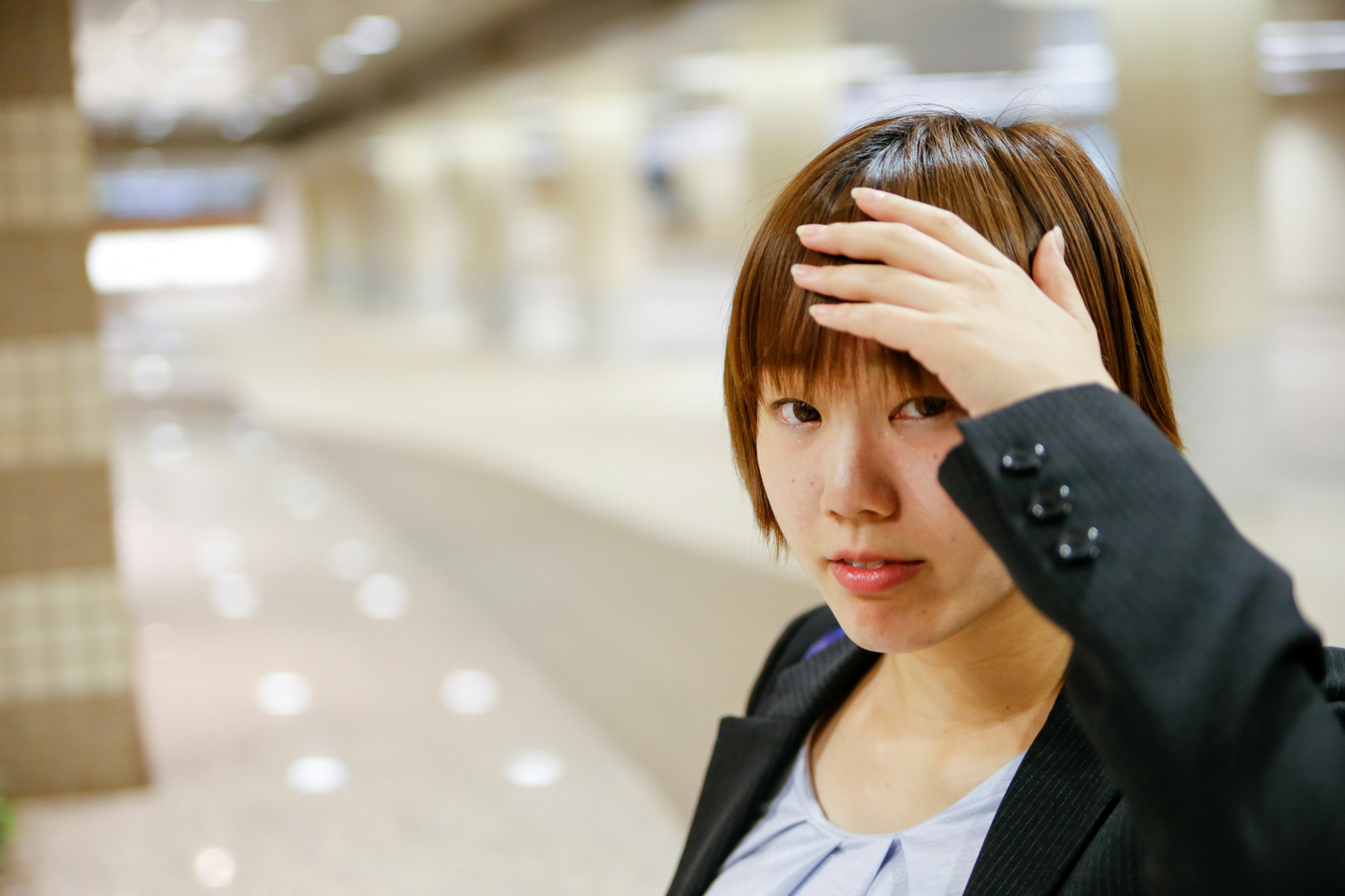 A woman in a business suit touching her forehead