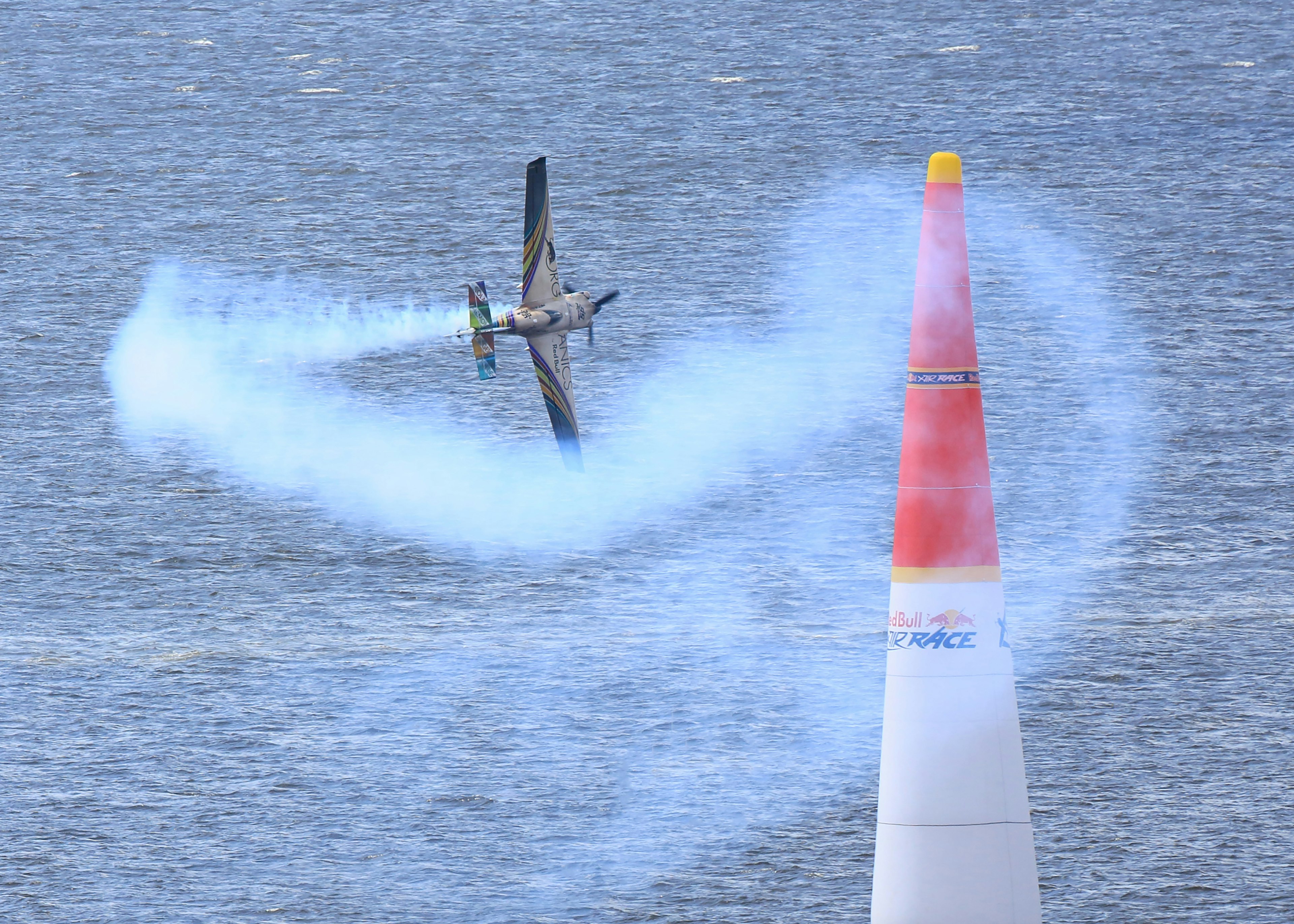 Akrobatikflugzeug führt über Wasser mit Rauchspur