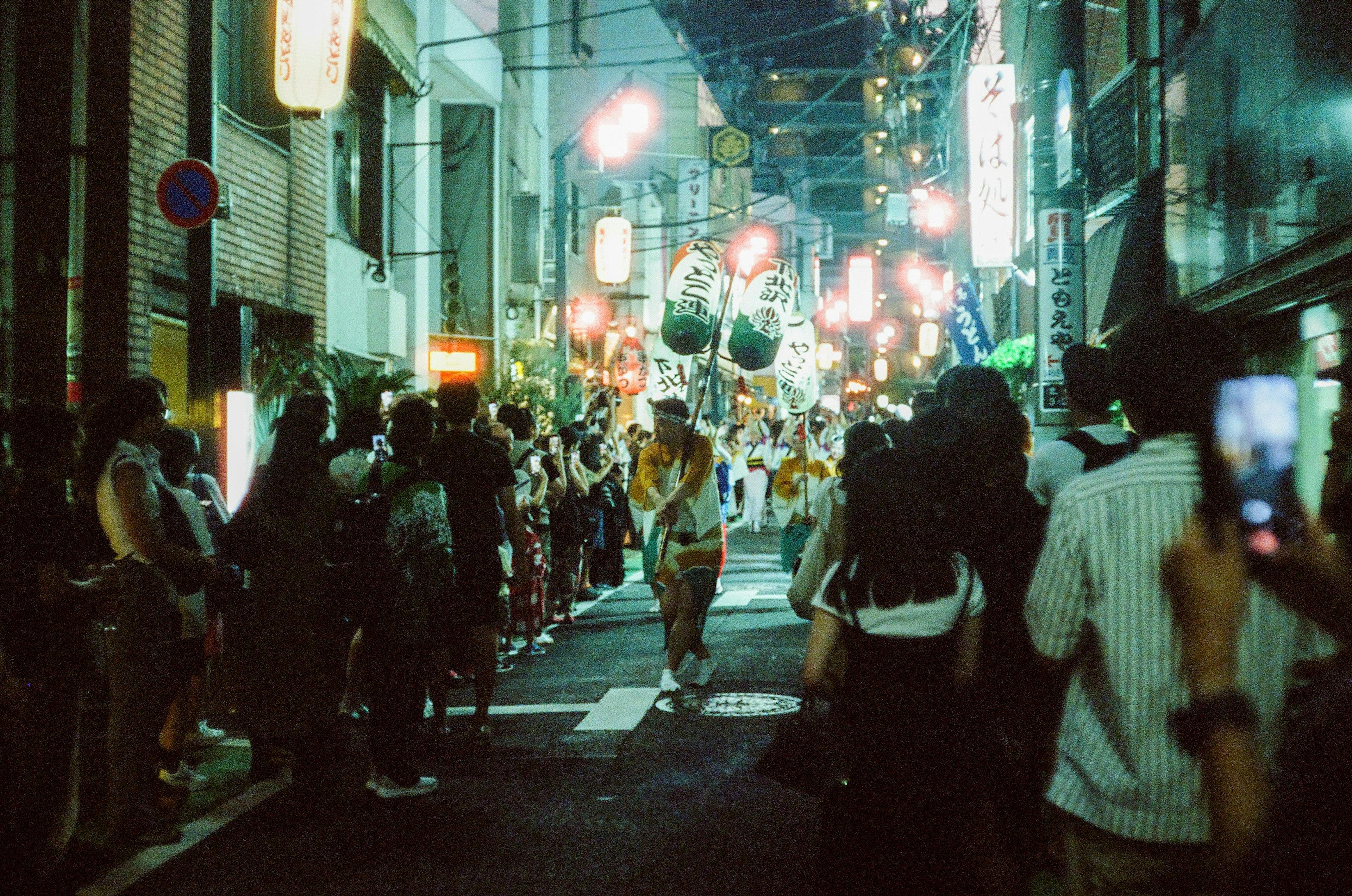 夜の祭りの行列が賑やかな通りを進む様子多くの観客が見守る中で色とりどりの提灯が照らす