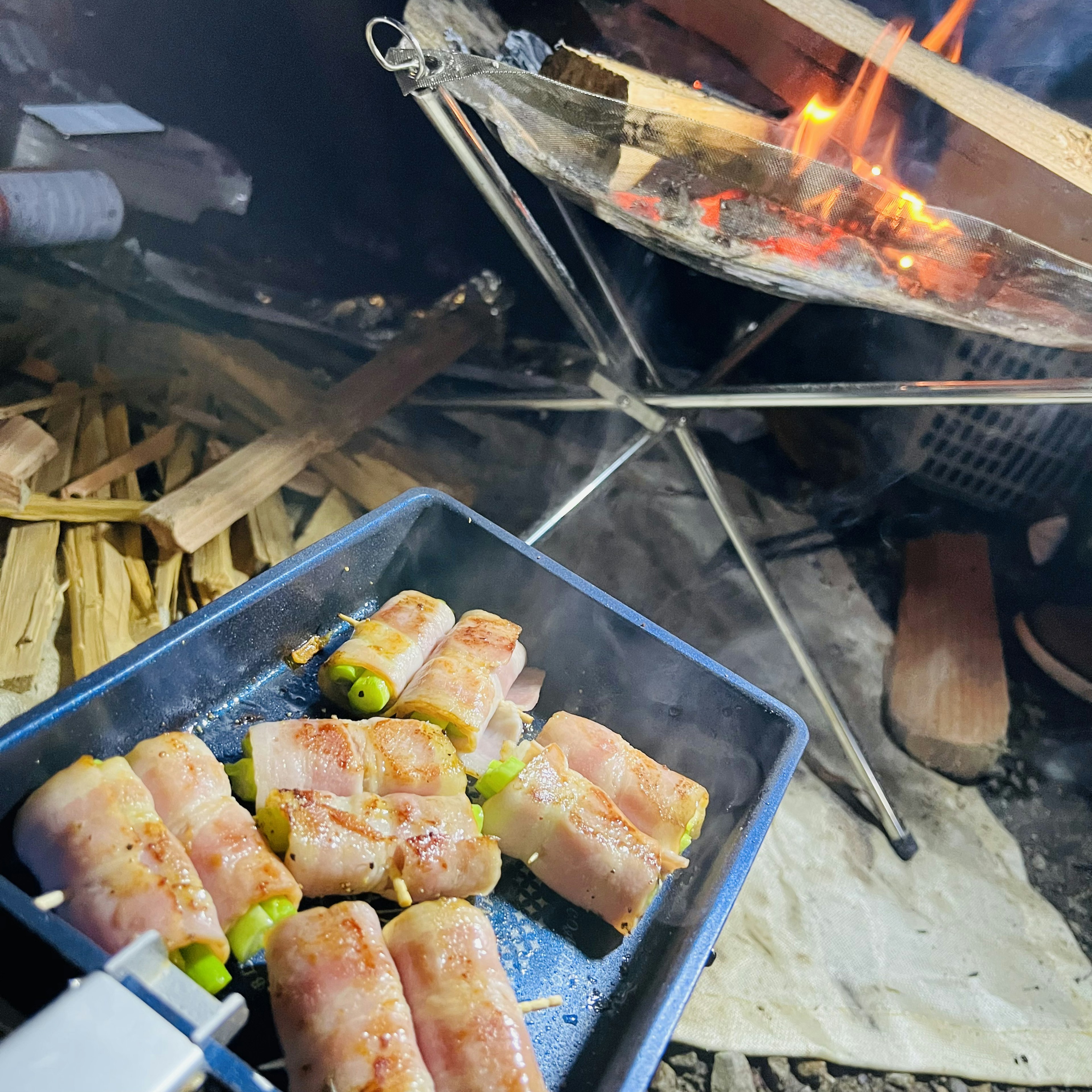 キャンプファイヤーの近くで焼かれているベーコン巻きの料理