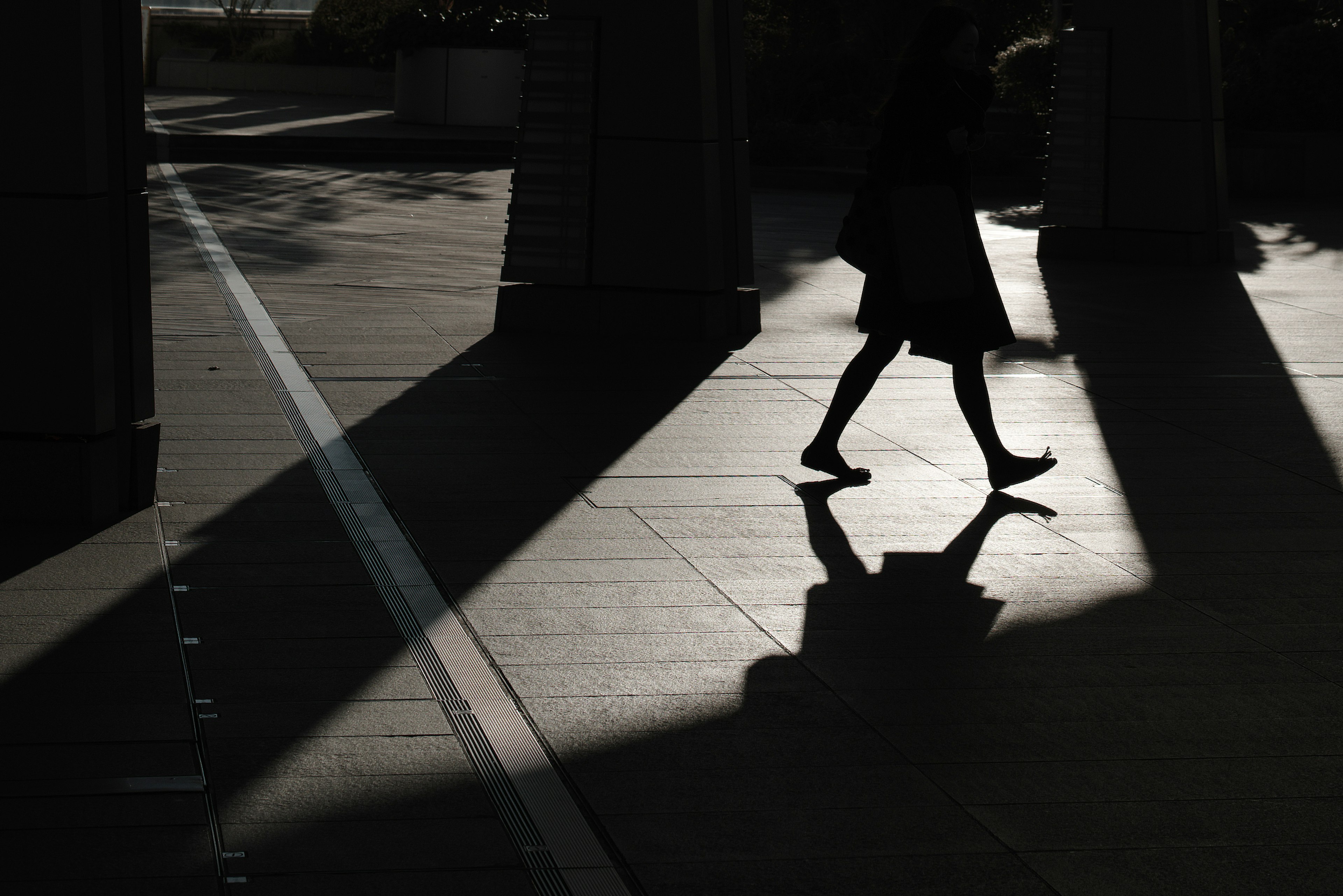 Silhouette di una persona che cammina su un pavimento illuminato dal sole