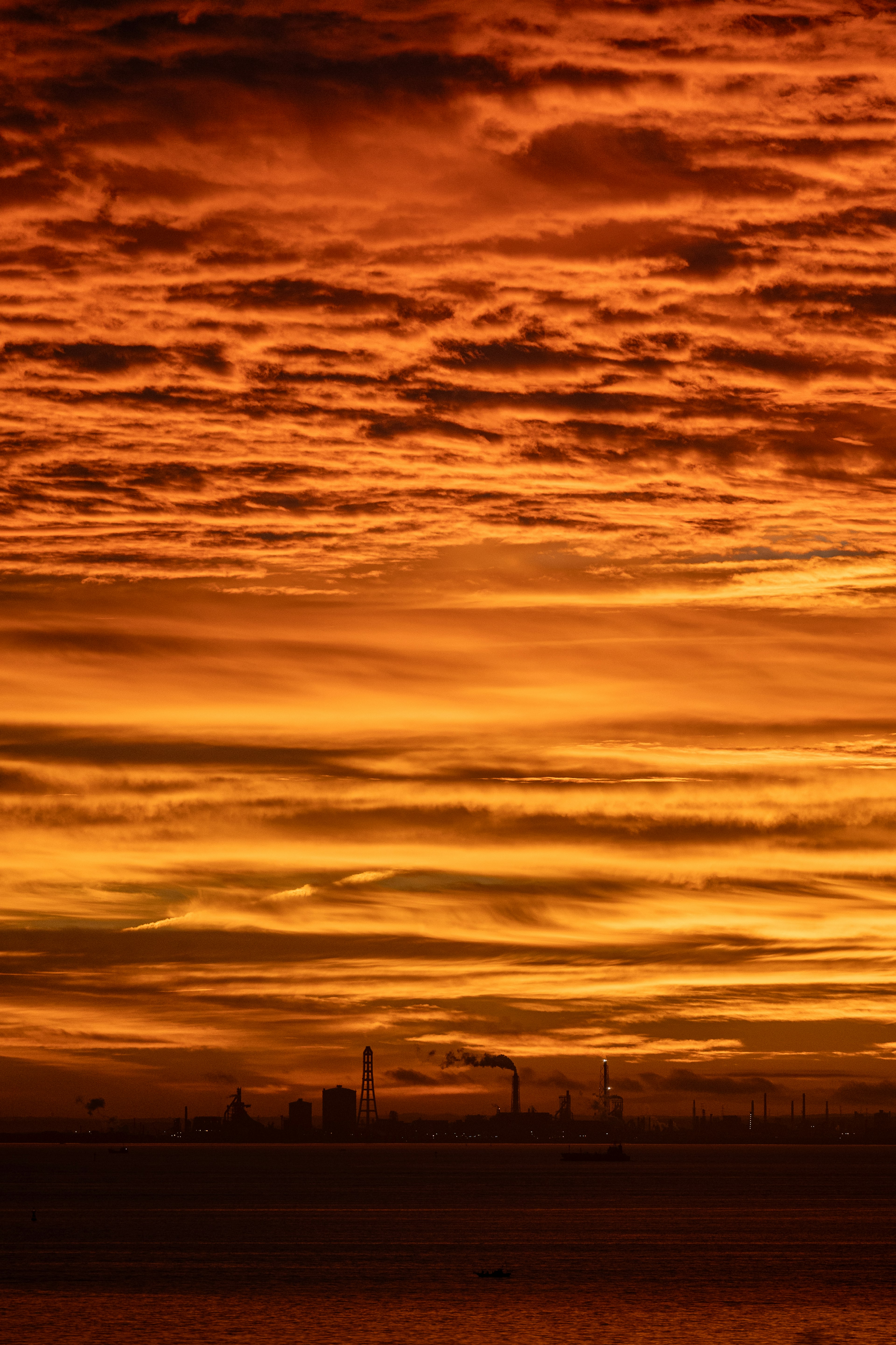 Langit senja oranye cerah dengan siluet pabrik