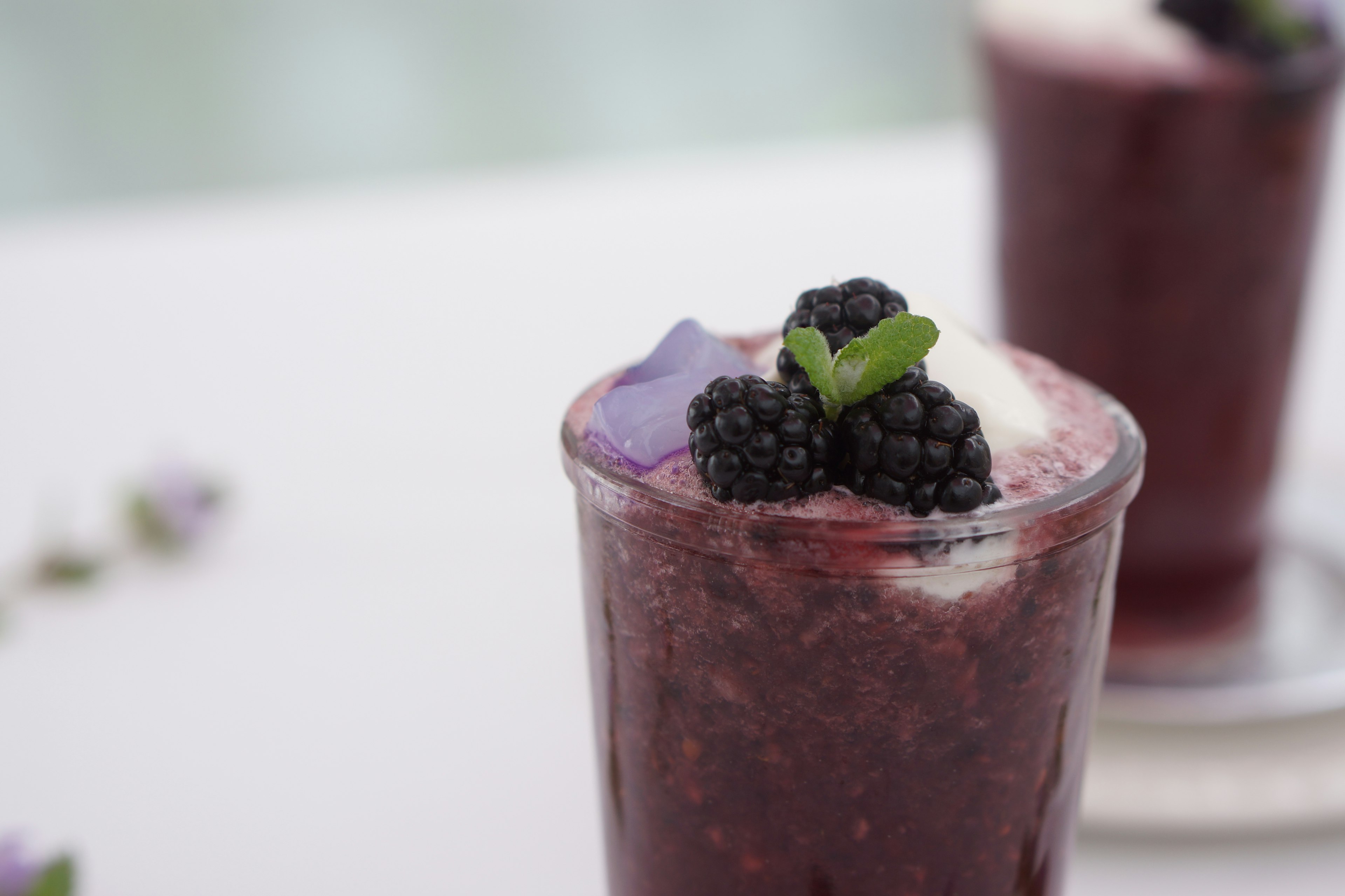 A smoothie glass topped with blackberries and mint leaves