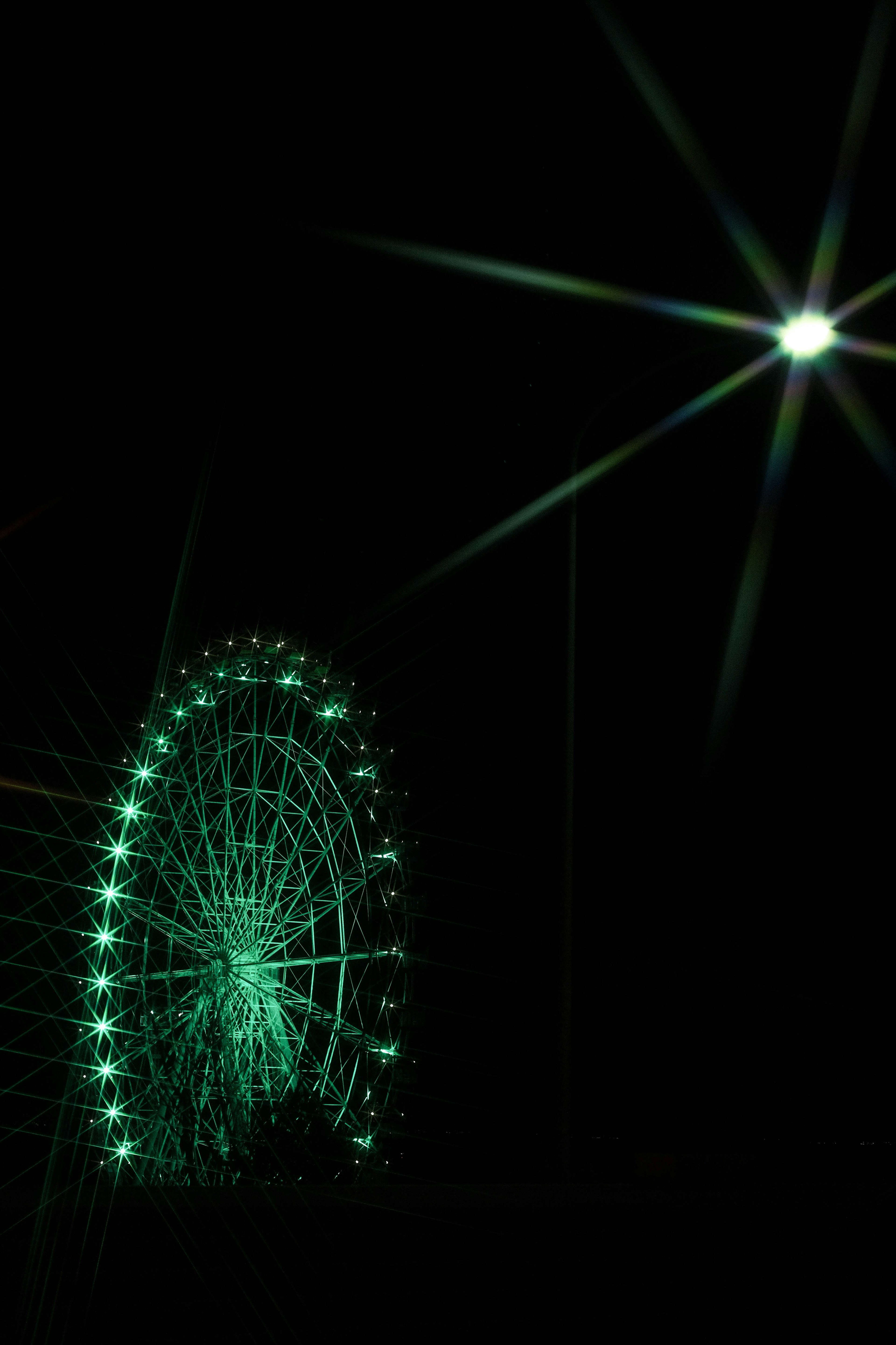 A beautiful scene of a green ferris wheel lit against a dark sky with a bright star-like light