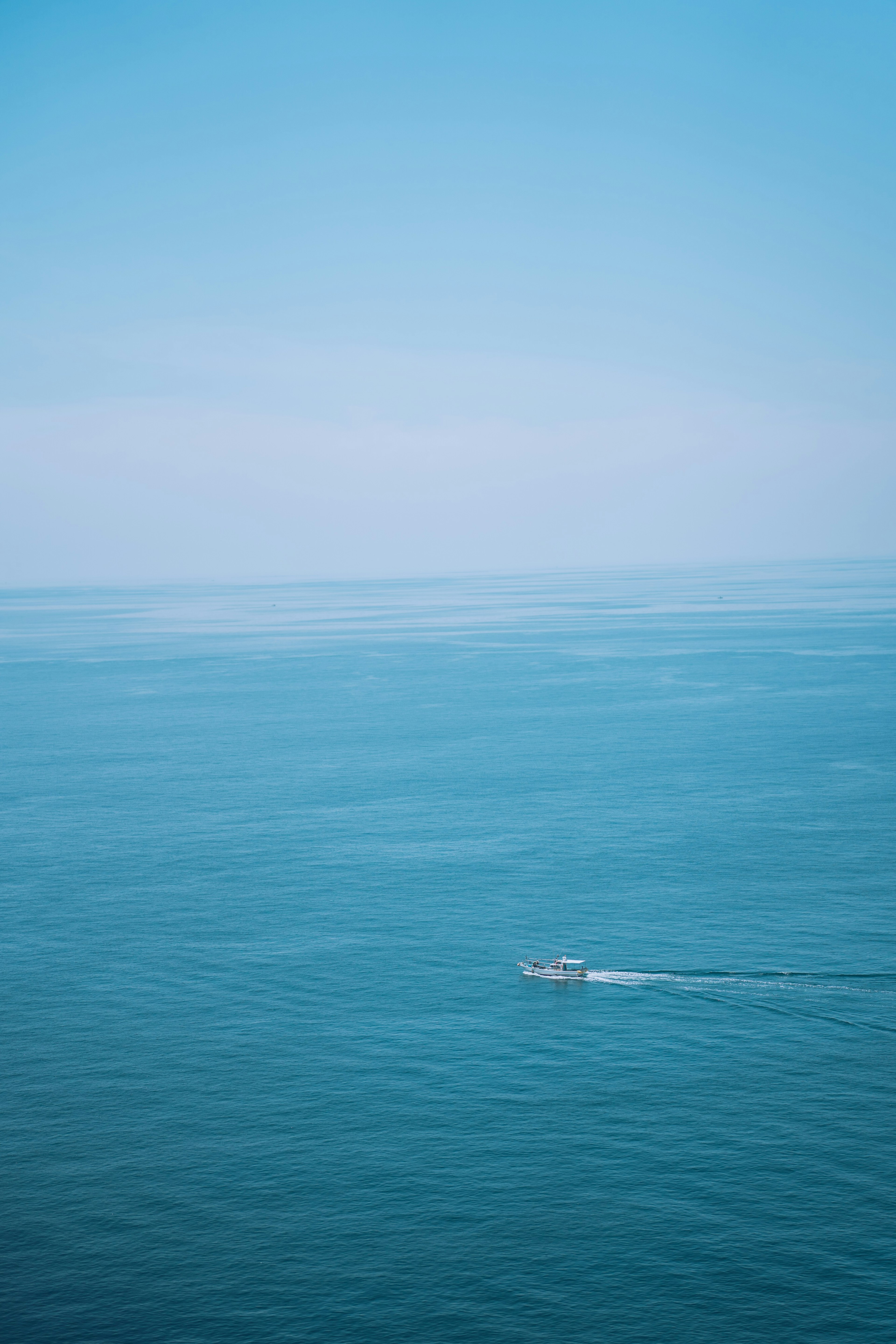 A small boat is gliding across a blue ocean under a clear sky