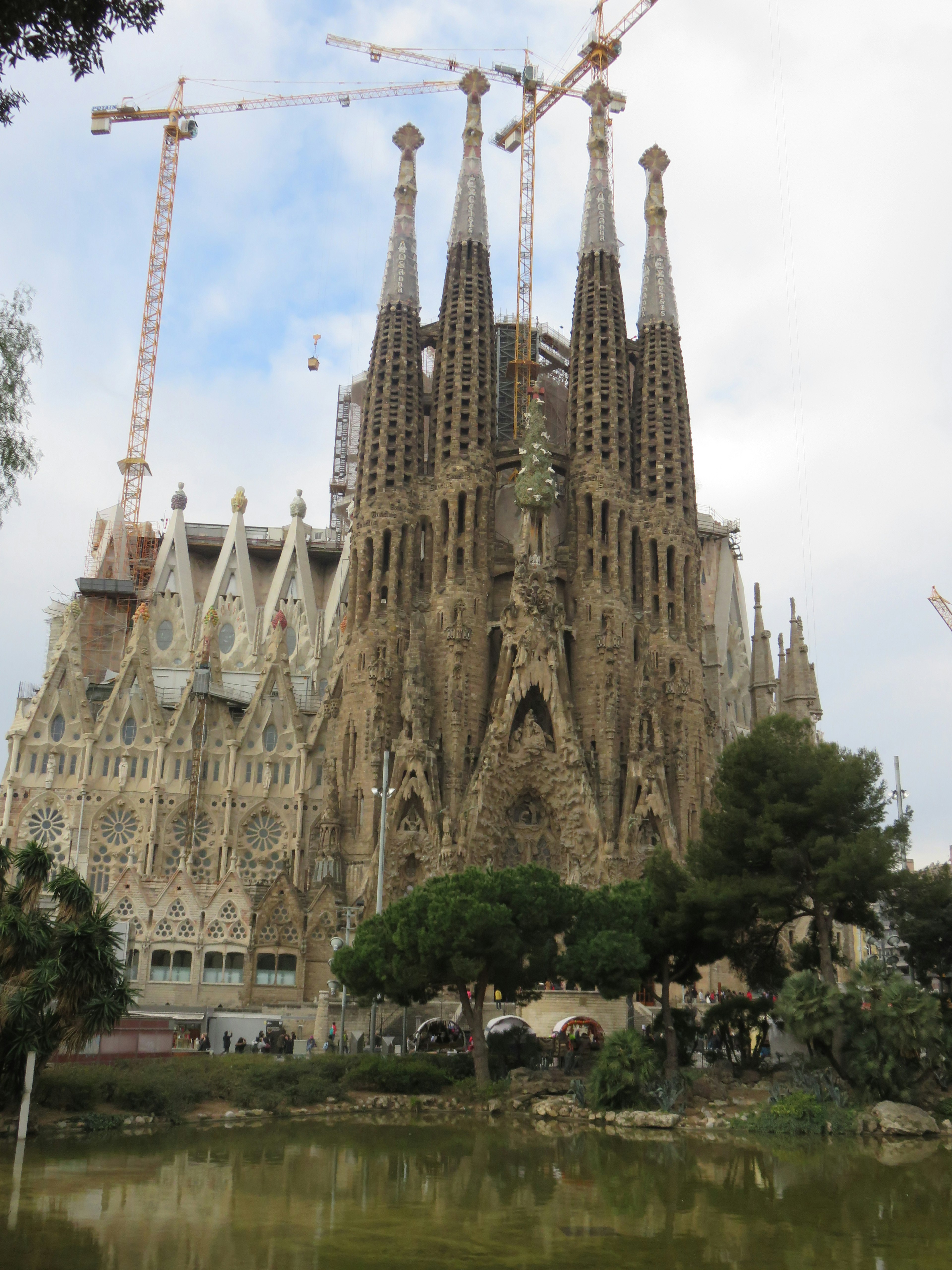 Sagrada Familia đang xây dựng với các tháp và cần cẩu xung quanh có cây xanh