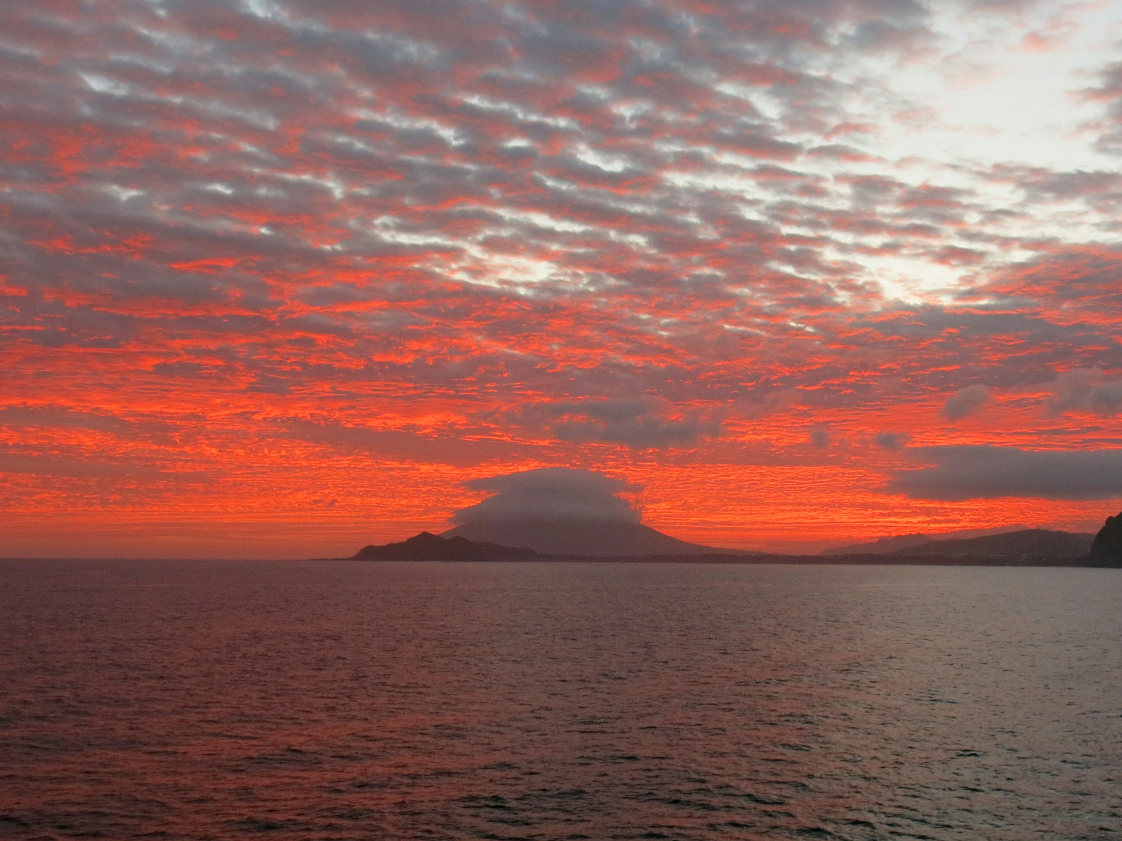 美しい夕焼けが海の上に広がり雲が赤く染まっている