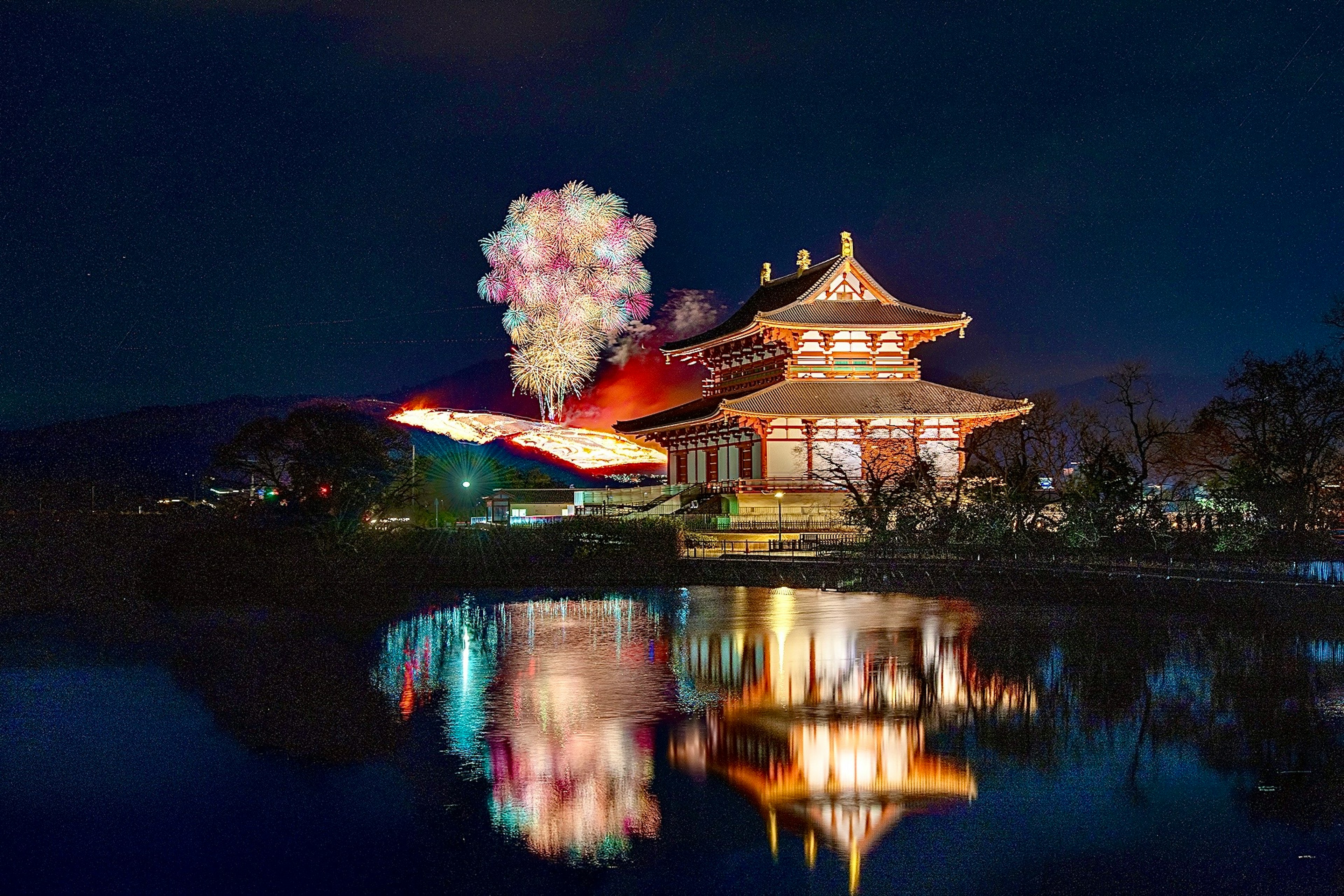 Un bâtiment traditionnel japonais se reflétant sur un lac la nuit avec des feux d'artifice dans le ciel