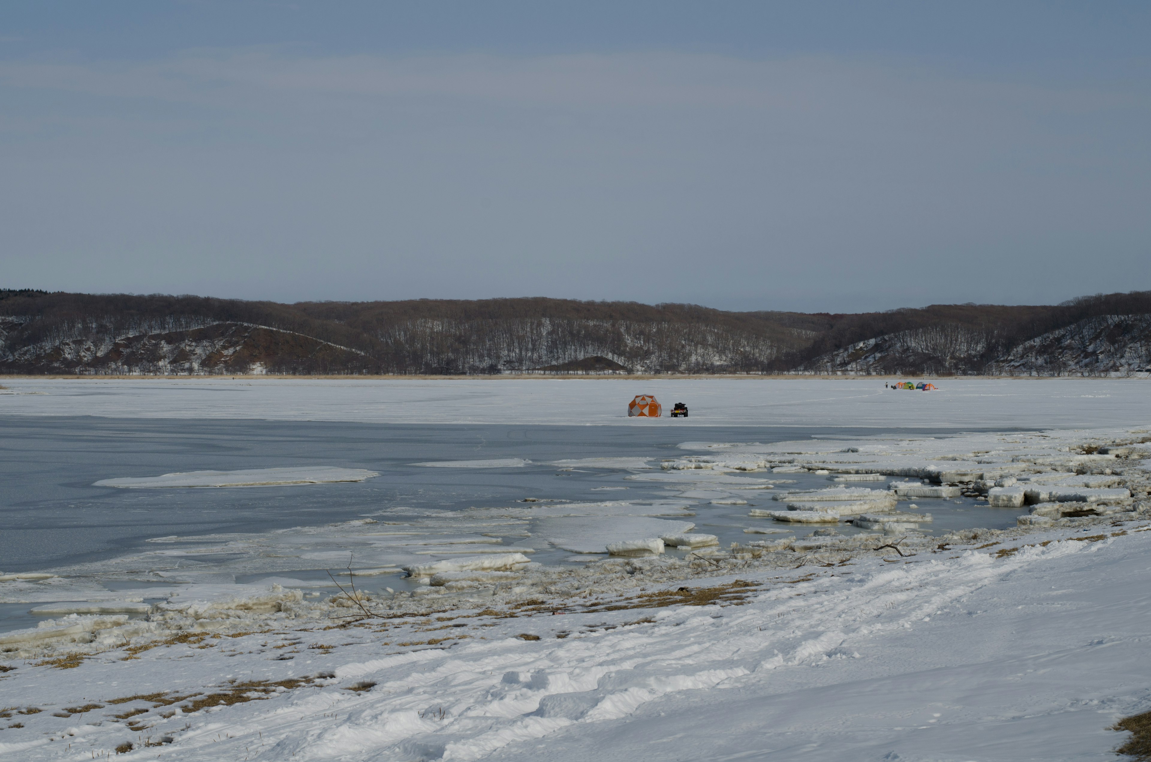 Paysage de lac gelé avec rivage enneigé petites cabanes visibles au loin