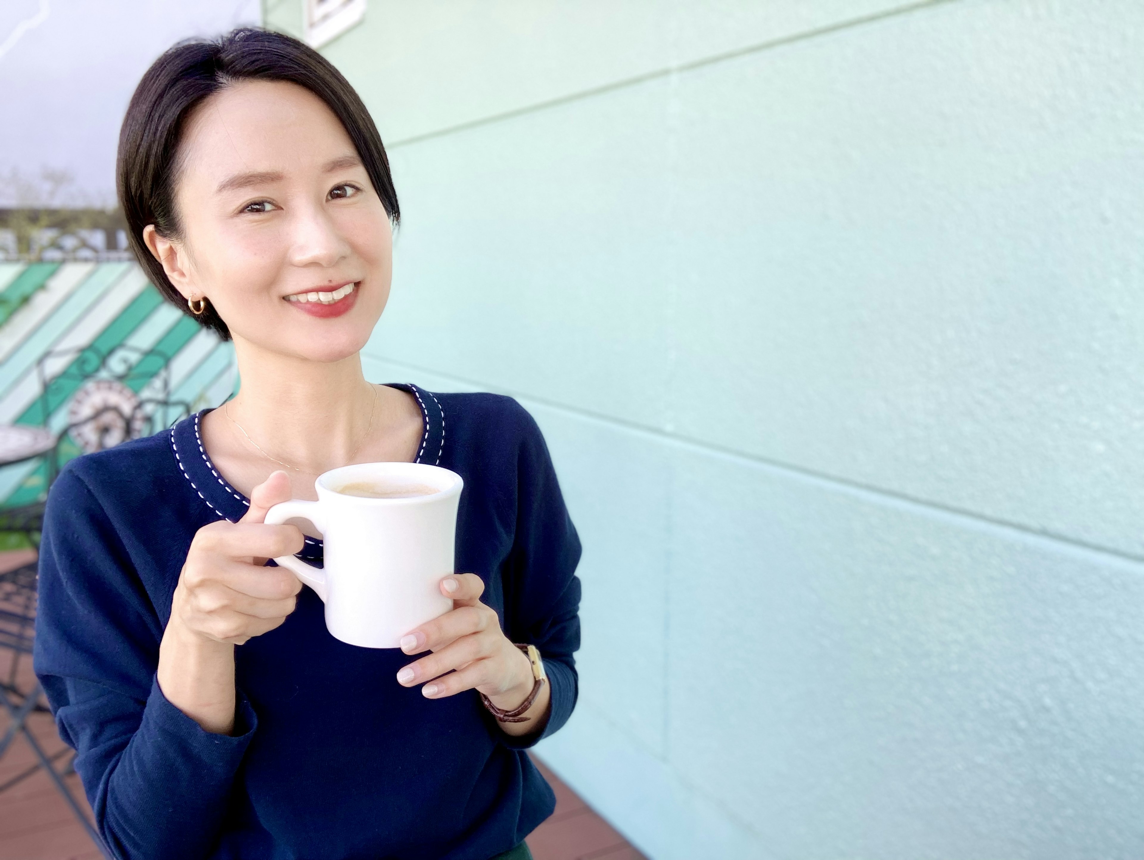 Frau lächelt und hält eine weiße Tasse vor einer blauen Wand