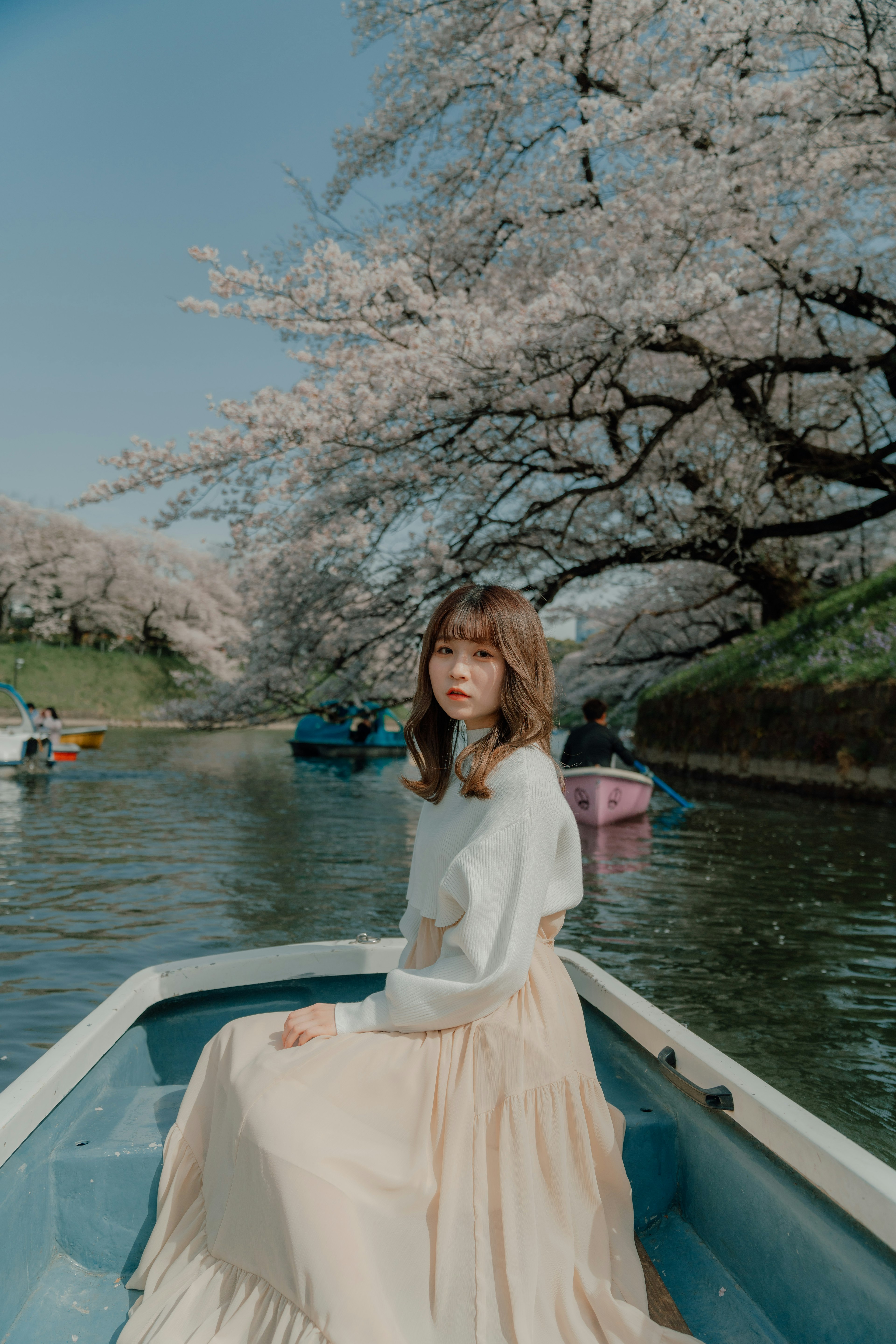 A woman sitting in a boat under cherry blossom trees