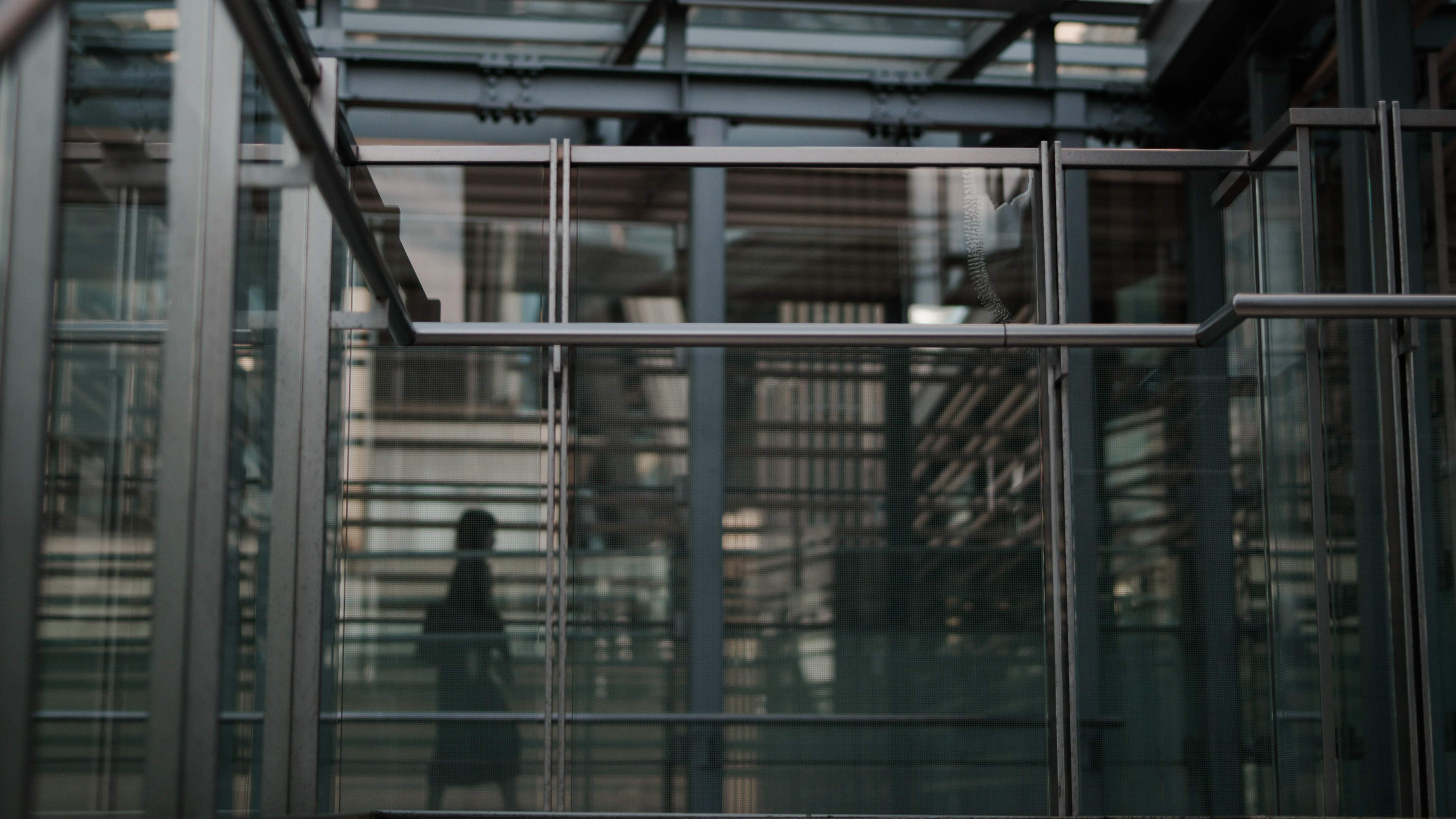 Silhouette d'une personne à l'intérieur d'une structure en verre et en métal avec un arrière-plan urbain