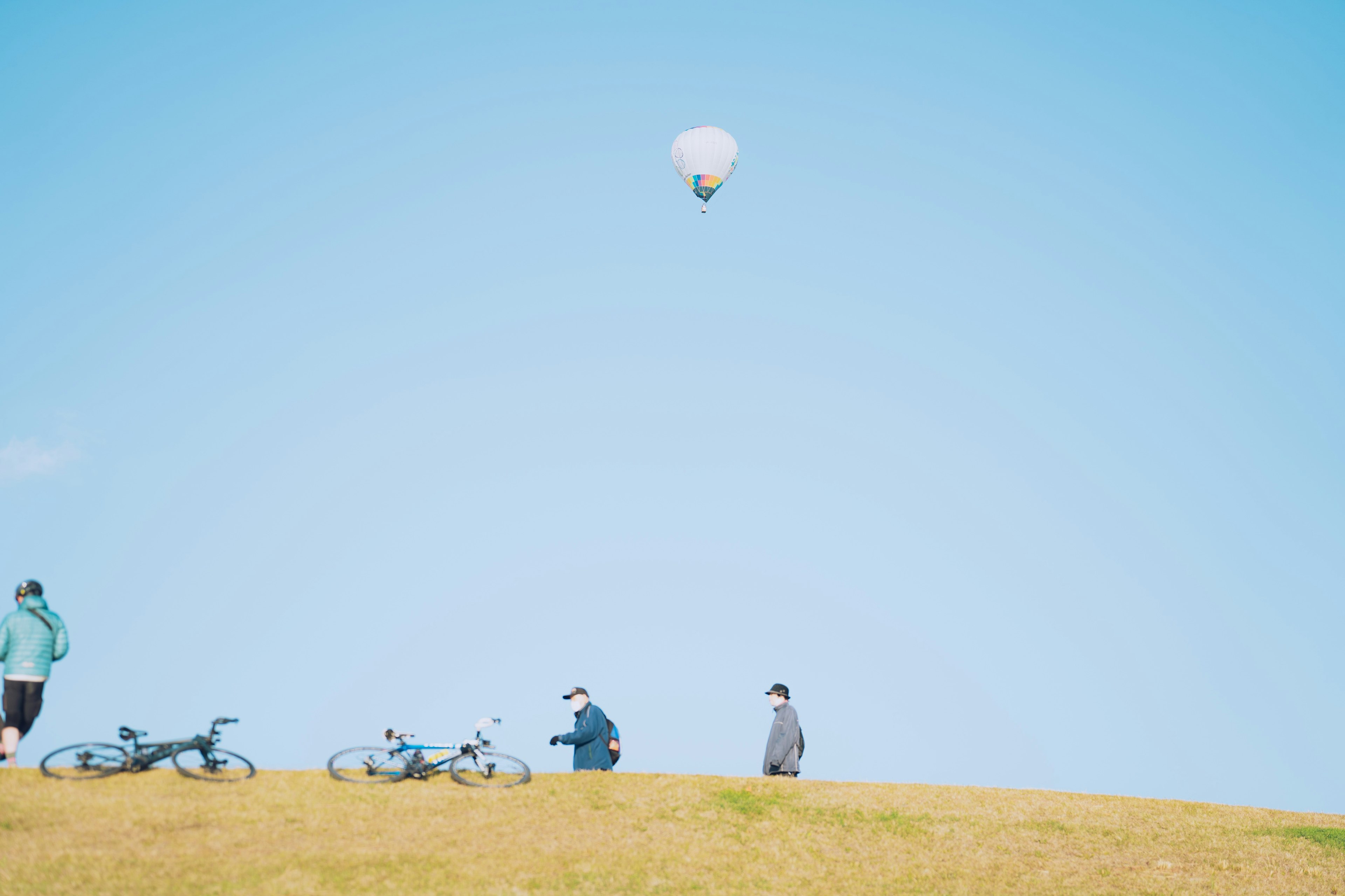 青空の下で風船が浮かぶ丘の上の人々と自転車