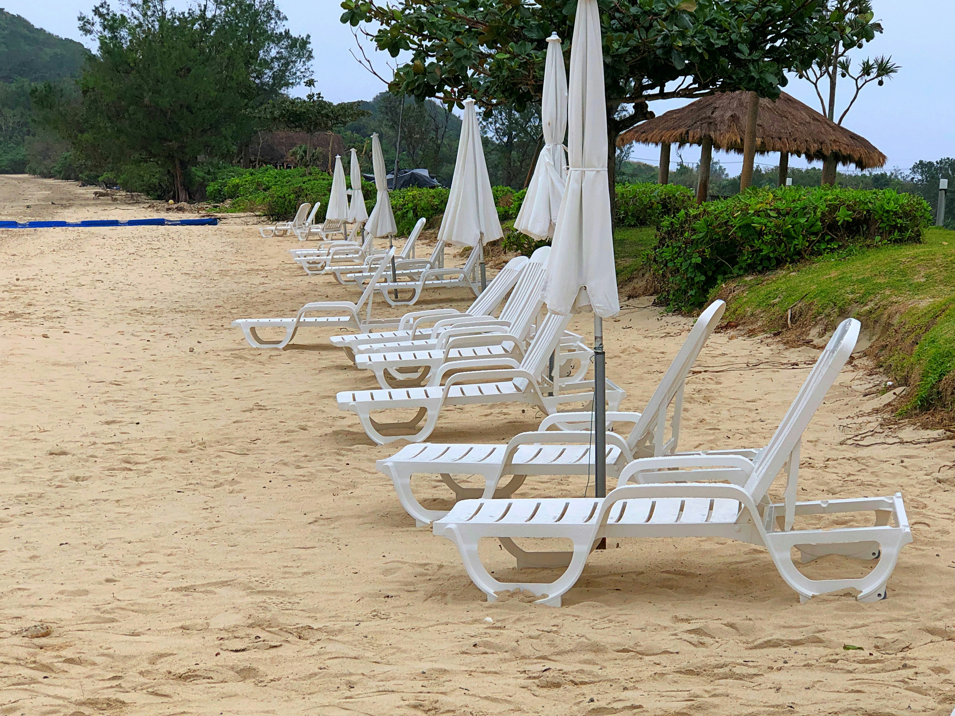 Strandszene mit weißen Liegen und Sonnenschirmen auf dem Sand