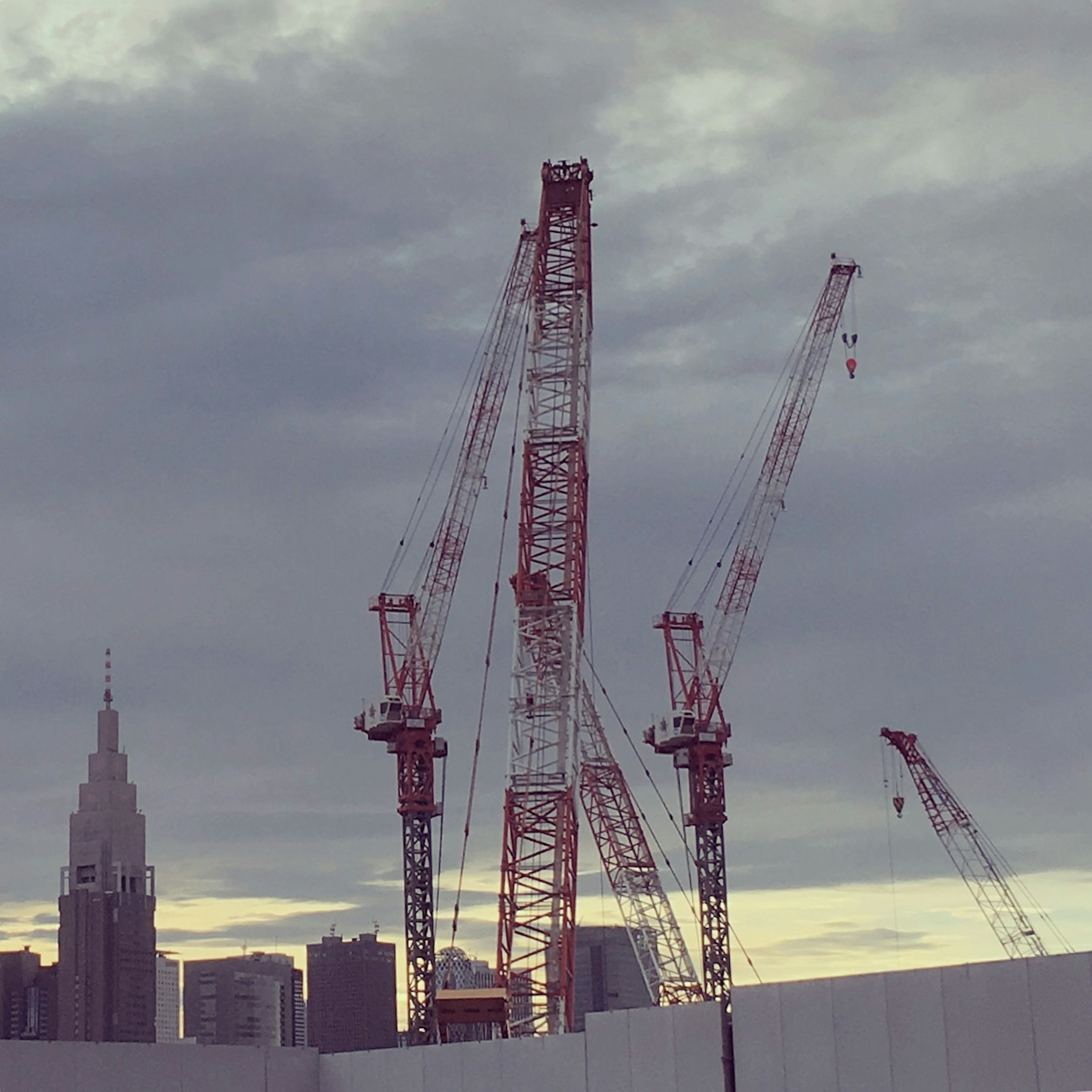 Red cranes at a high-rise construction site under a cloudy sky