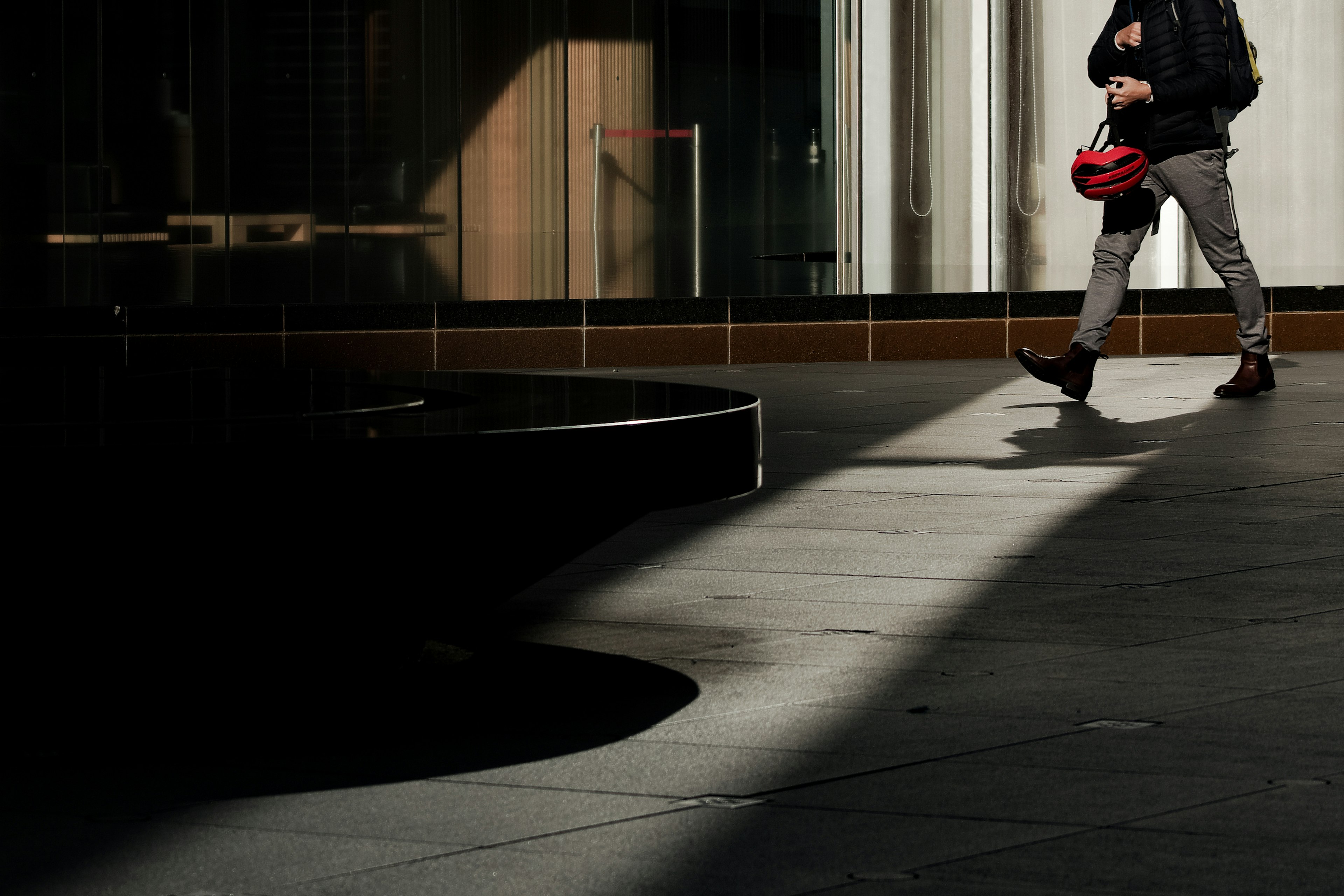 Una figura in ombra che cammina con una borsa rossa in un ambiente urbano con aree di luce e ombra contrastanti