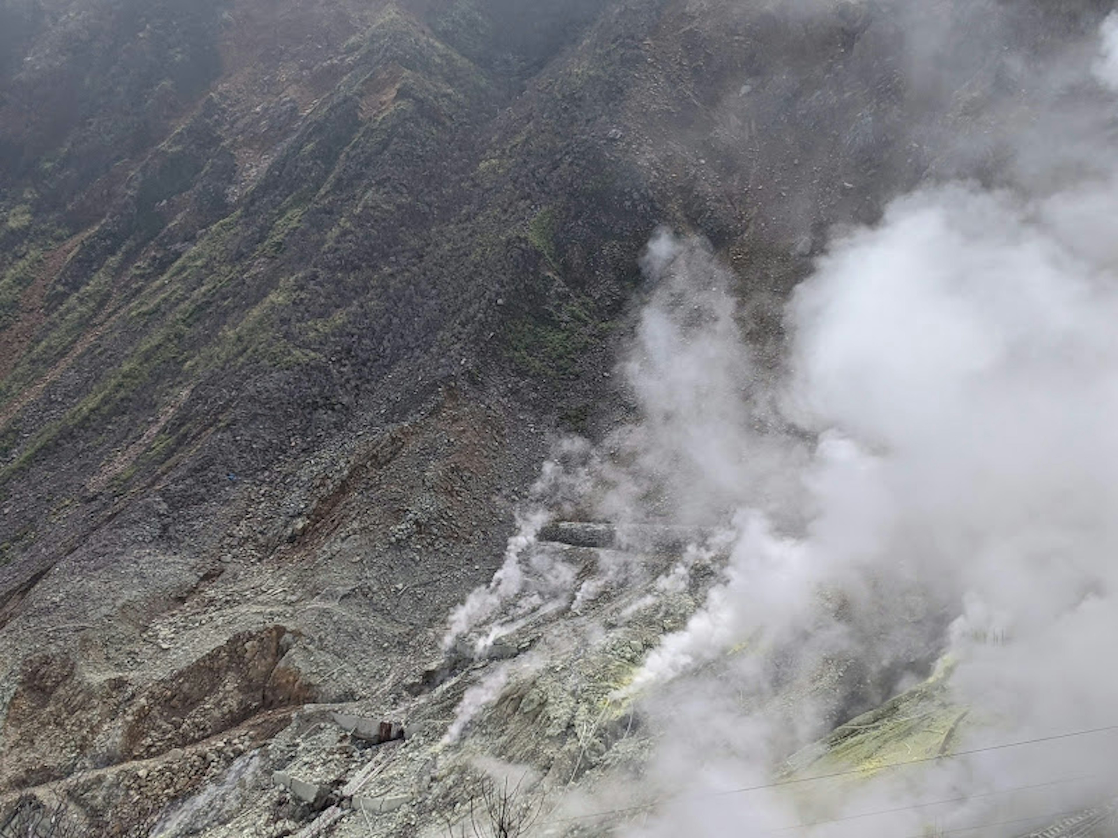 Volcanic slope emitting steam with greenish rocks