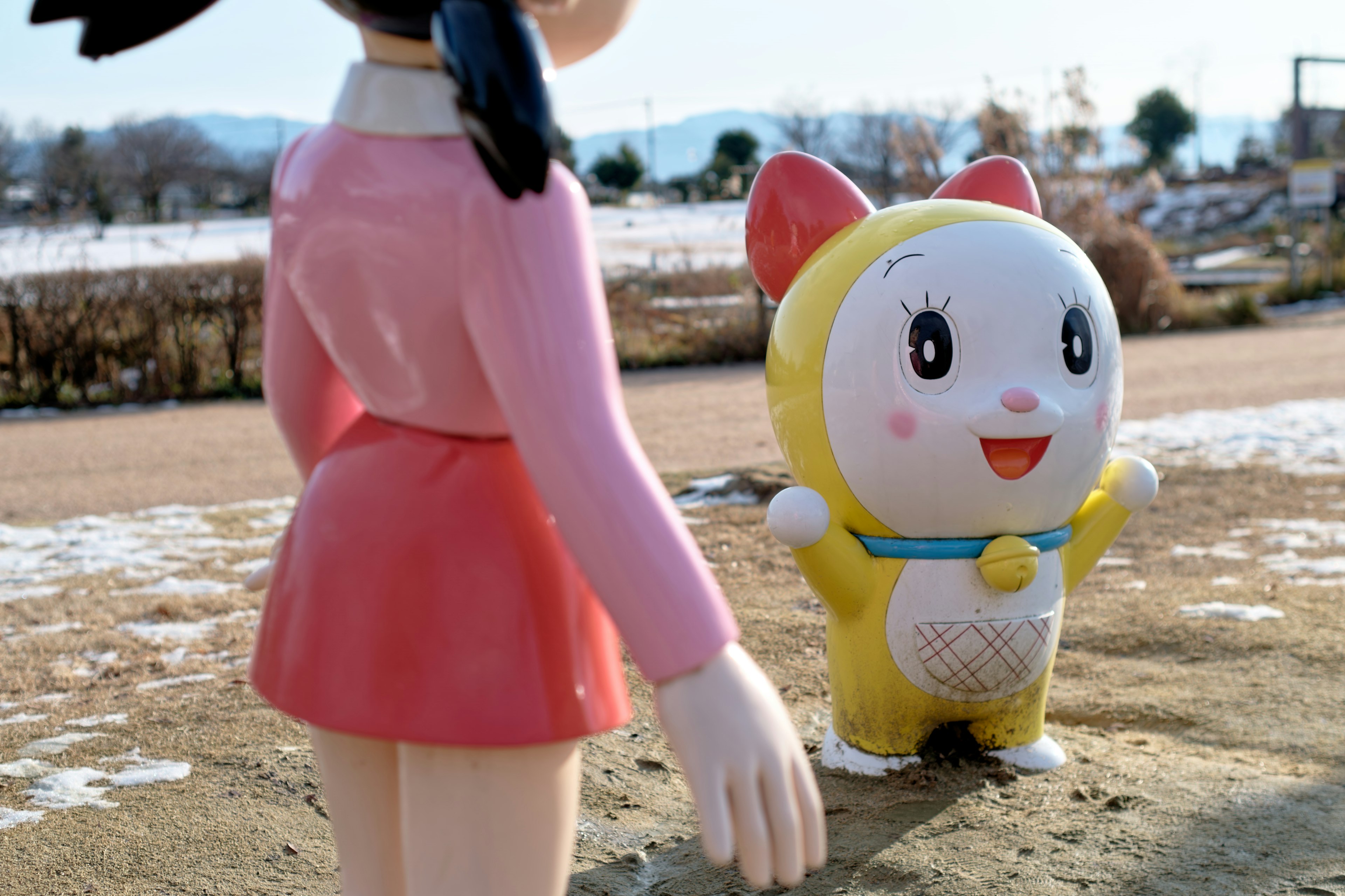 Une figurine de fille et une figurine de personnage jaune se tenant dans un parc