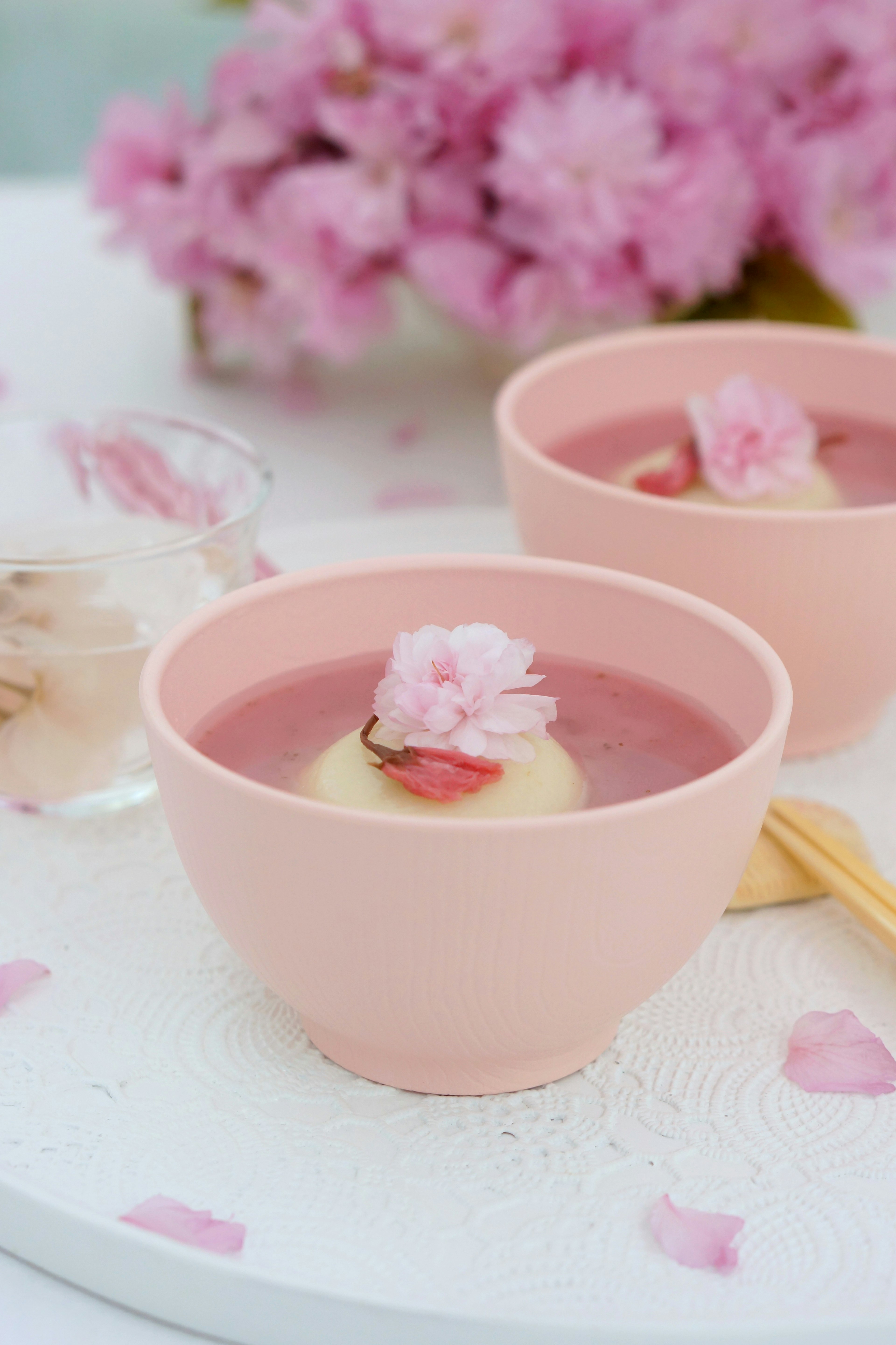 Two bowls of pink dessert with cherry blossoms floating on top