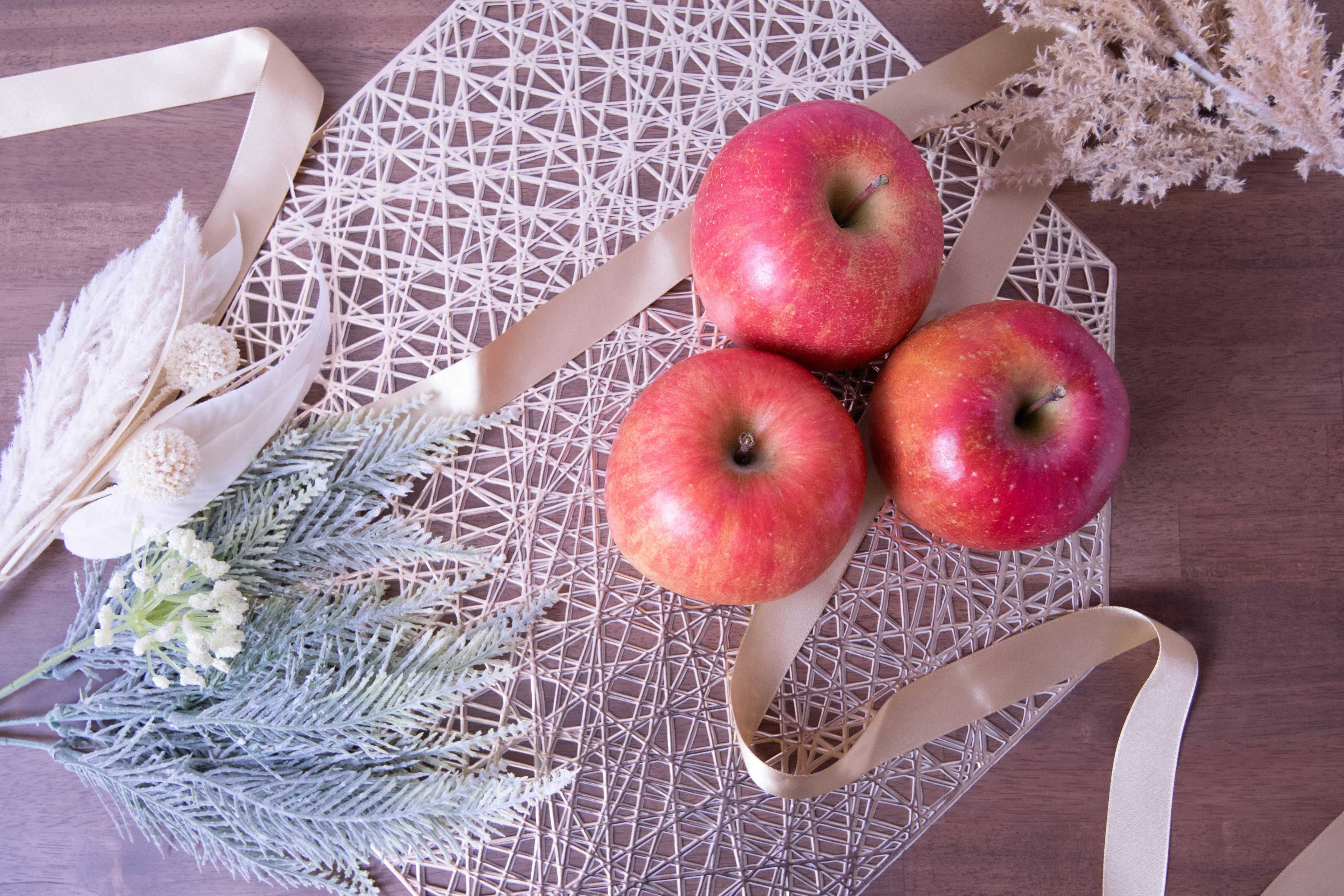 Tre mele rosse disposte con fiori secchi su un tavolo decorativo