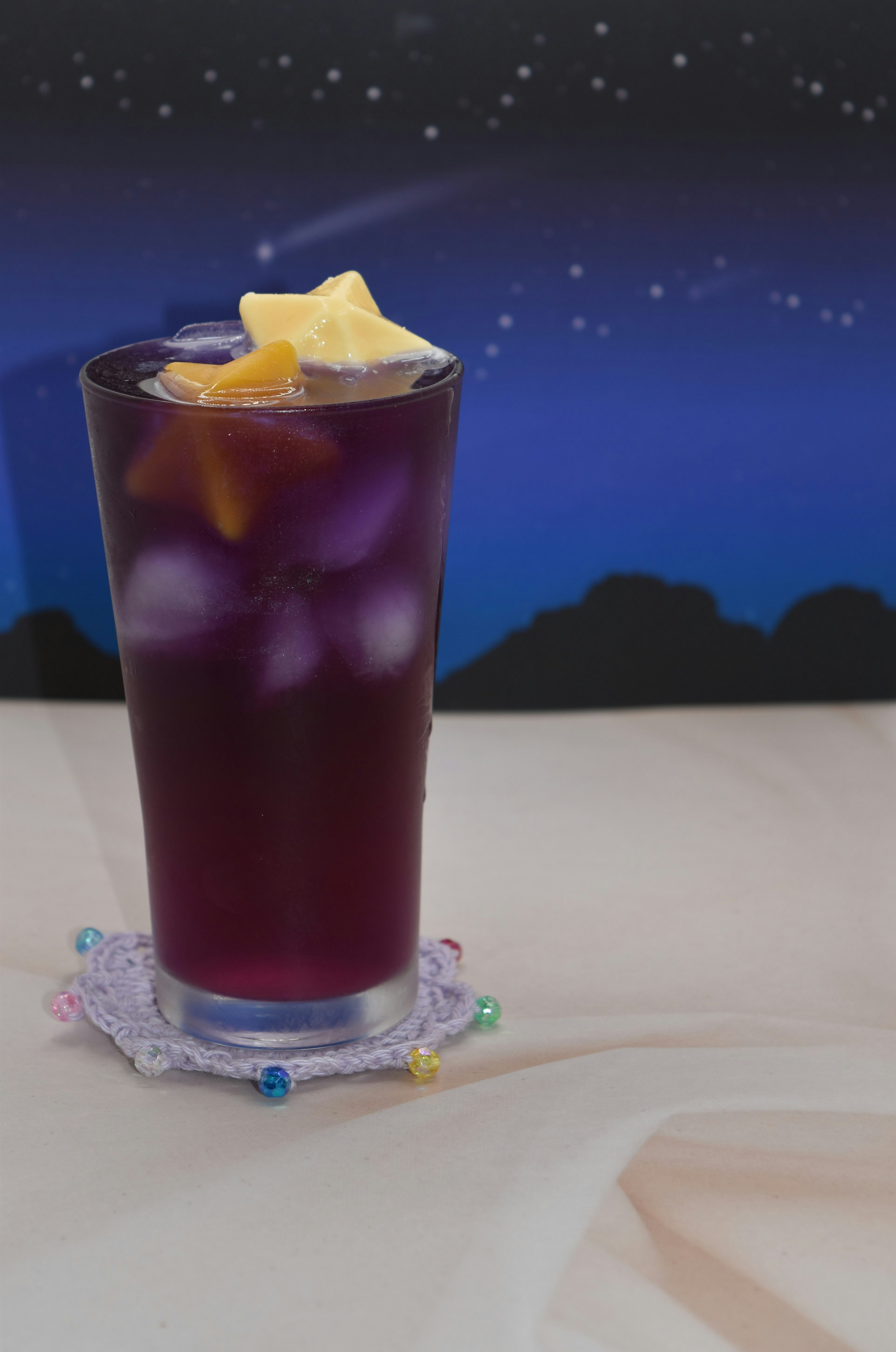 A purple drink with ice and star-shaped fruit garnish in a glass