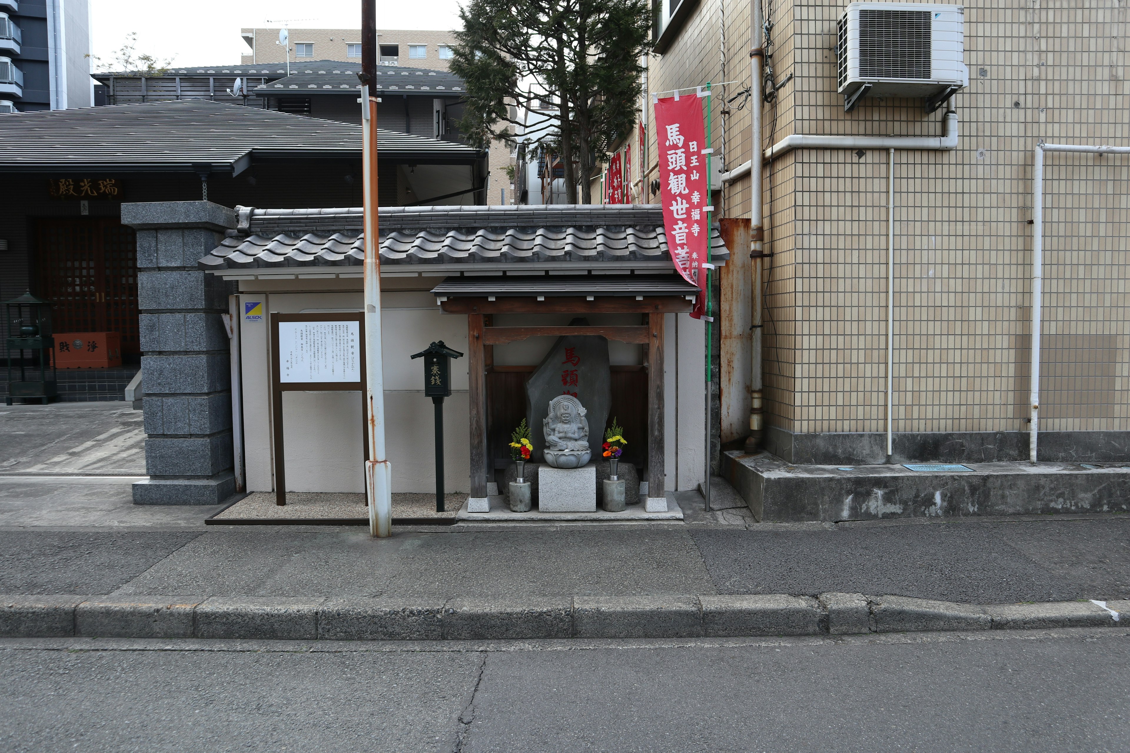 Entrance of a small shrine at the street corner with a stone statue and flower offerings