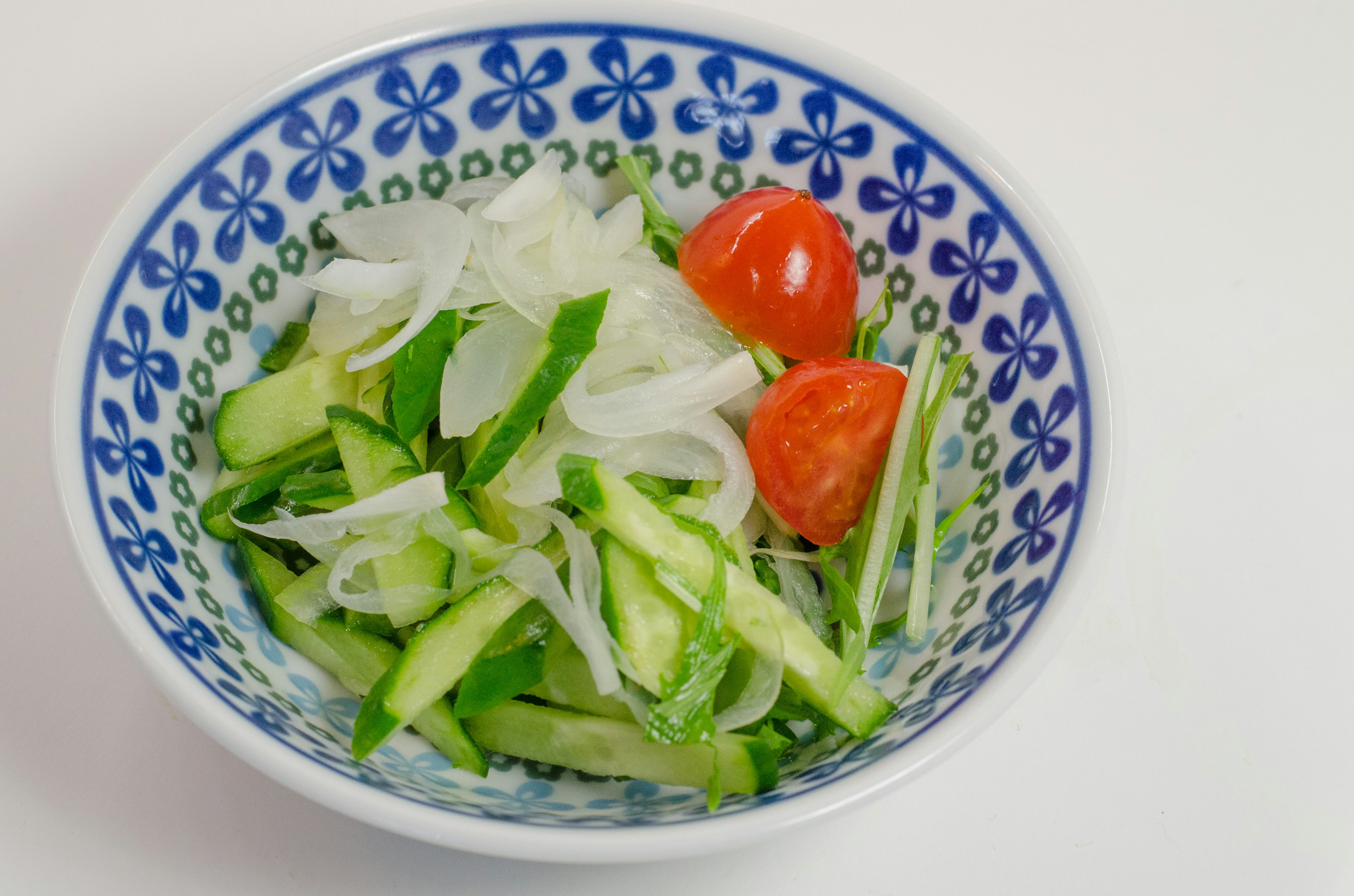 Frischer Gemüsesalat mit geschnittenen Gurken und Kirschtomaten in einer blauen Blumenschüssel