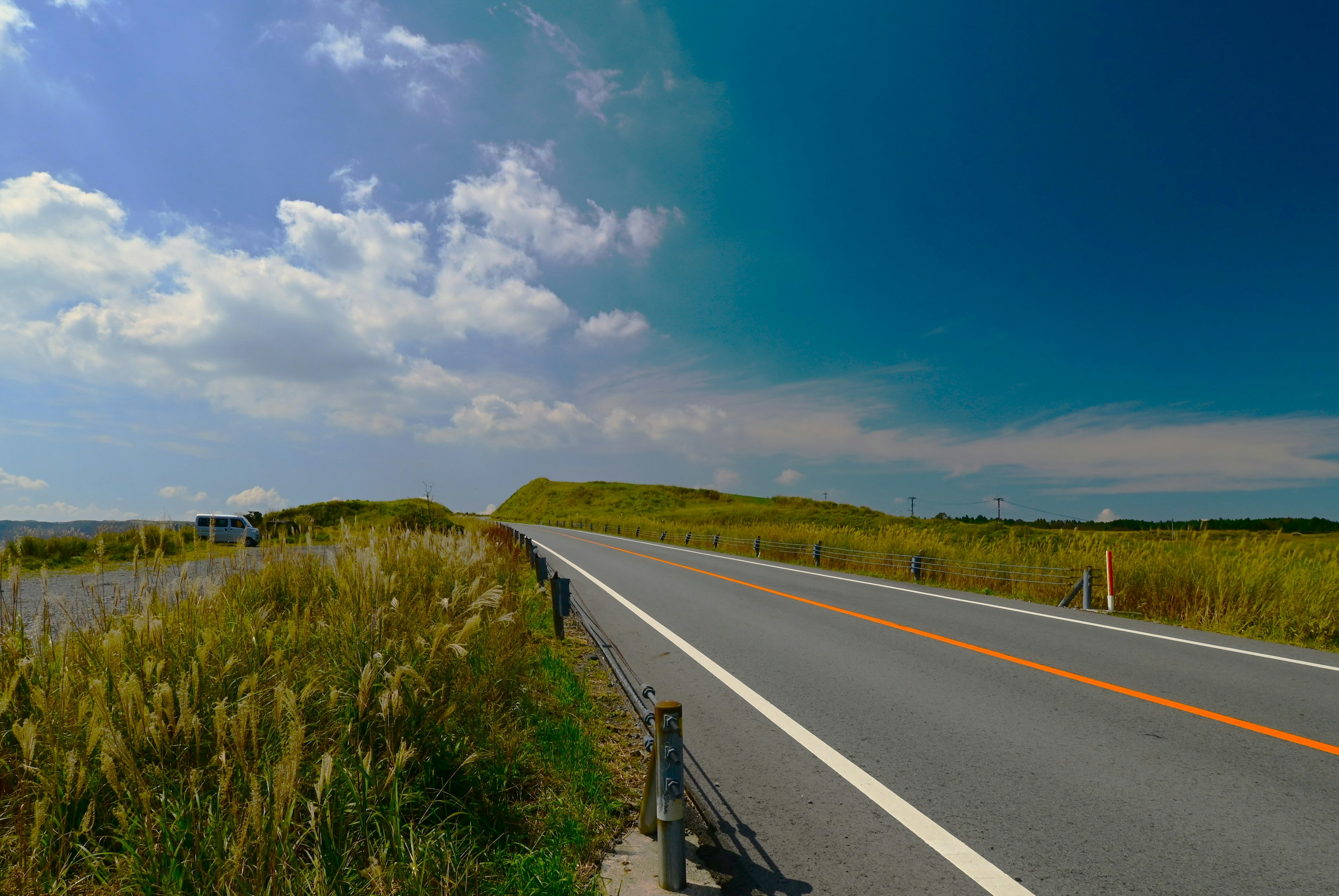 青空と雲が広がる風景の中に続く道路と草原