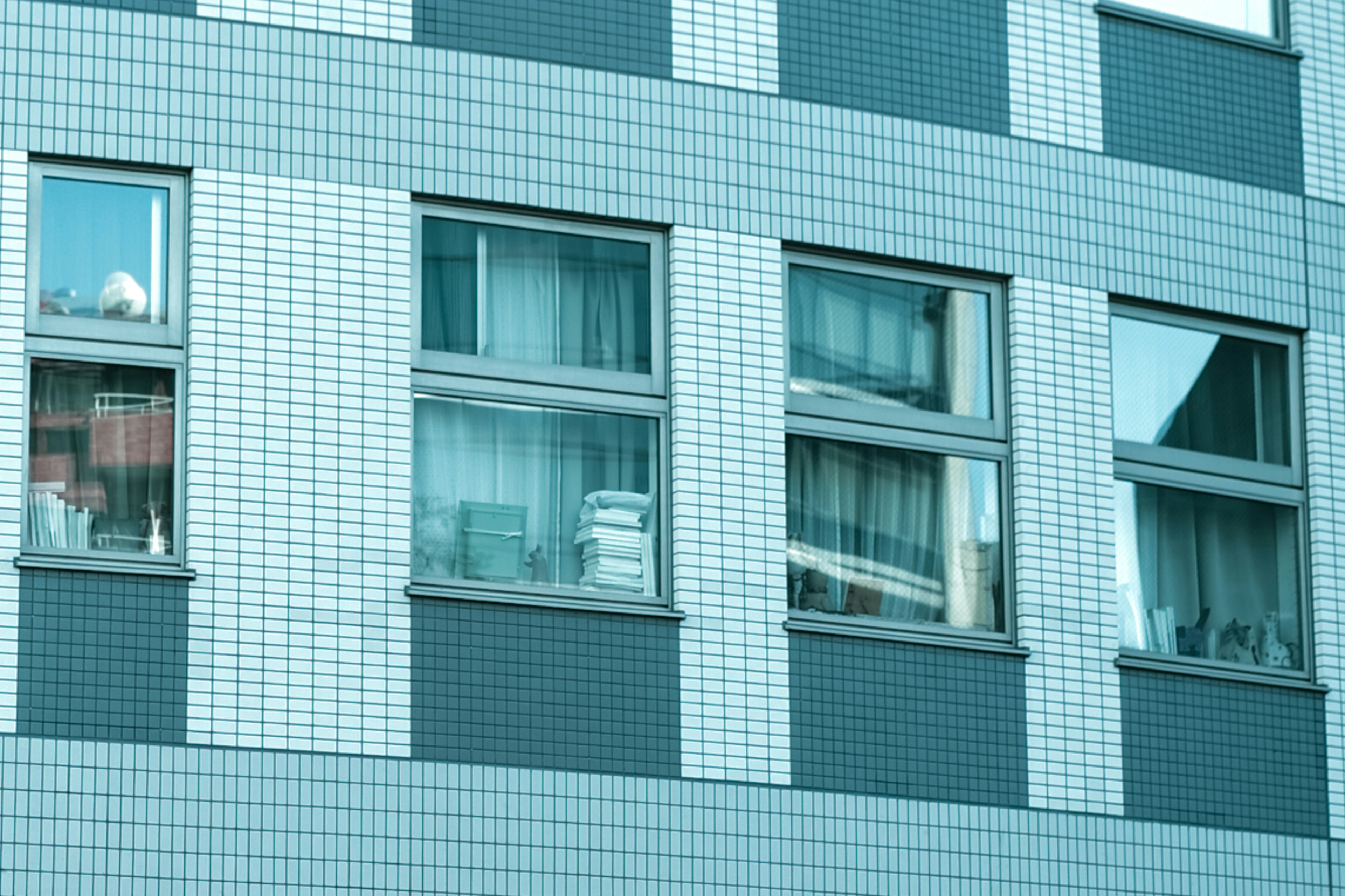 Section of a building with blue tiled exterior featuring windows and curtains