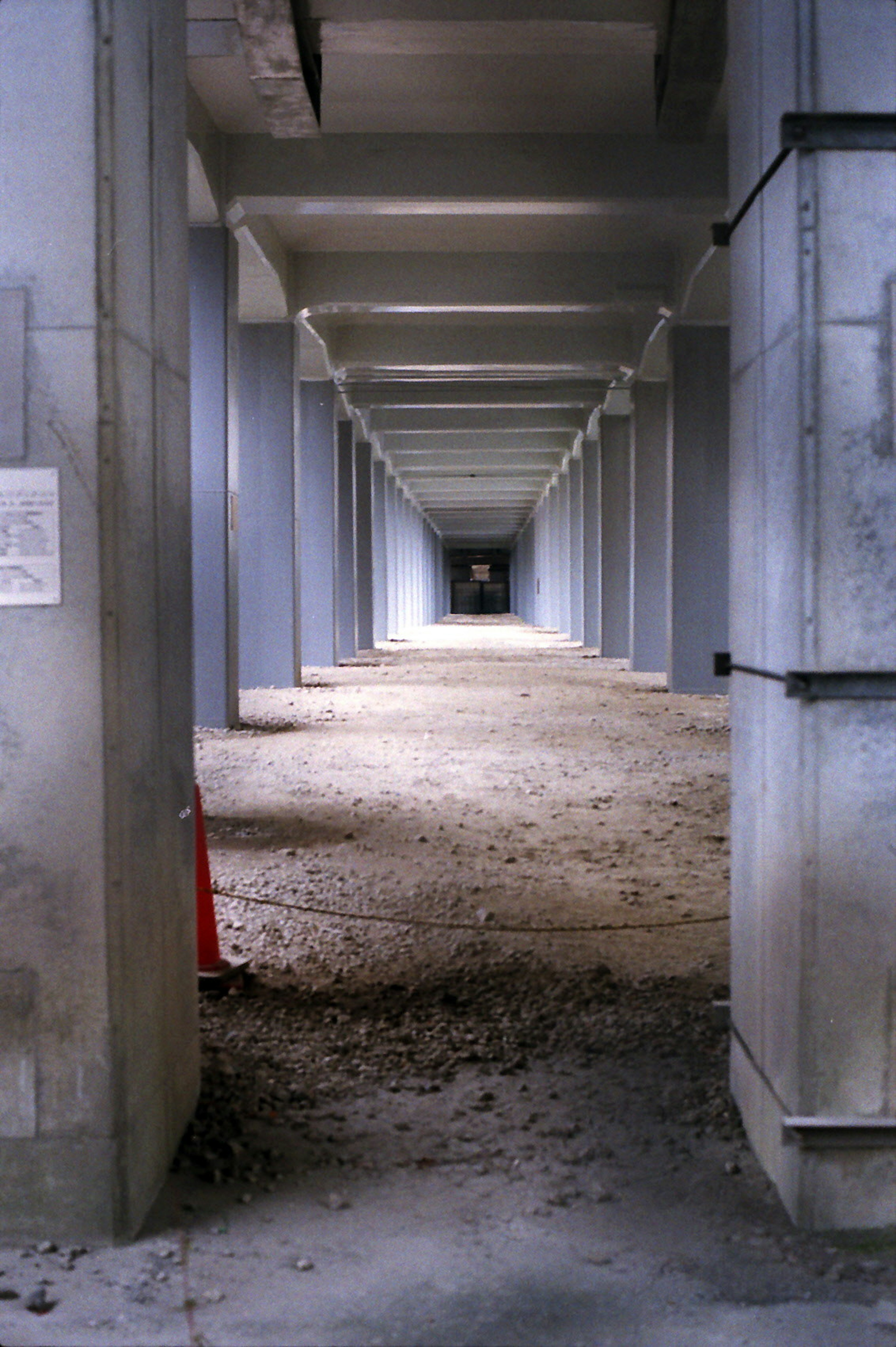 Long concrete arches create a corridor with a dirt floor and a red cone placed in the foreground