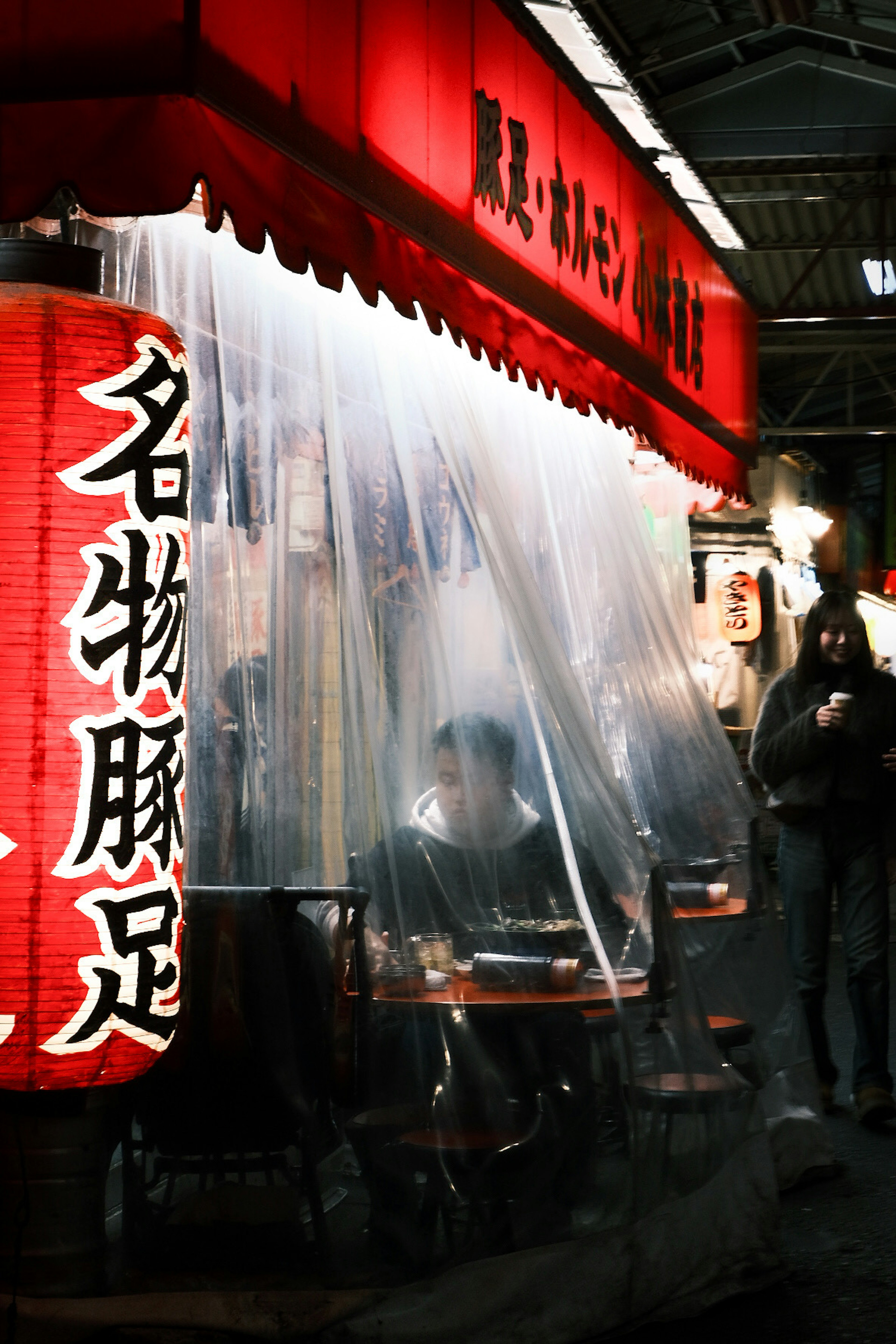 Street food stall with neon sign and transparent curtain covering tables