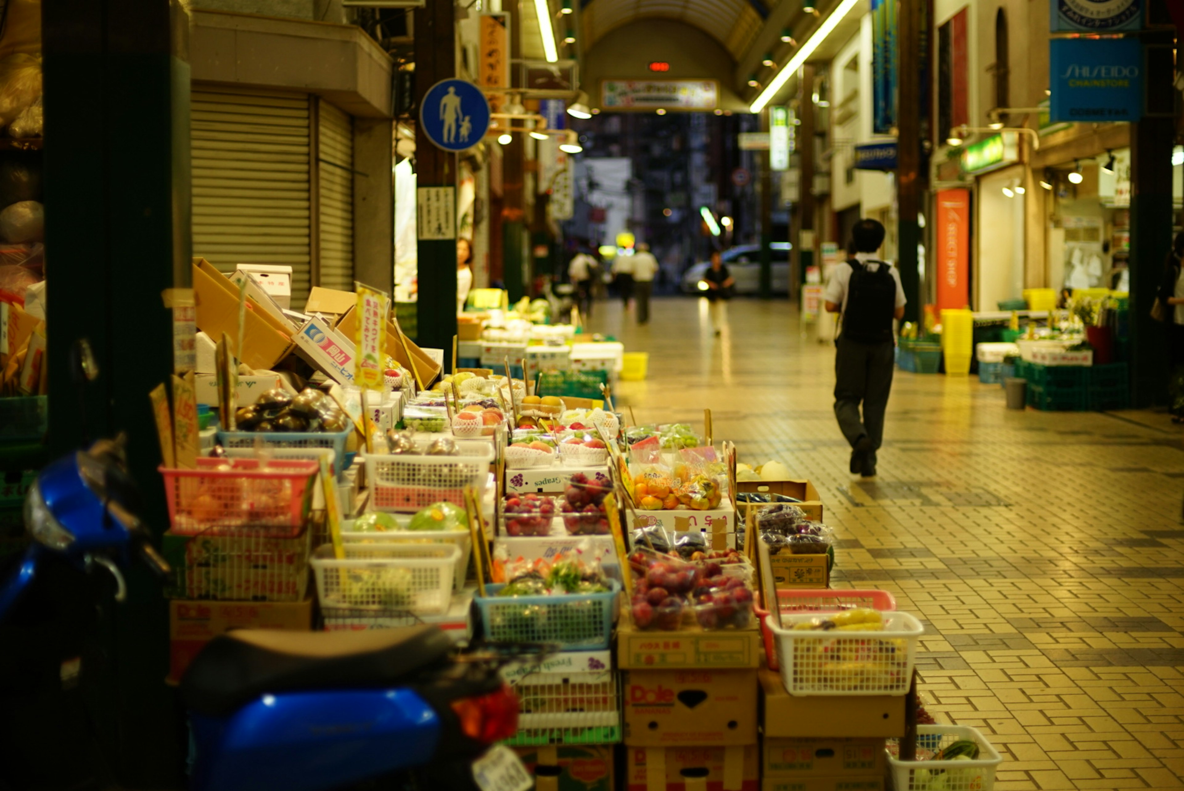 Puestos de frutas alineados en una calle del mercado con un peatón solitario