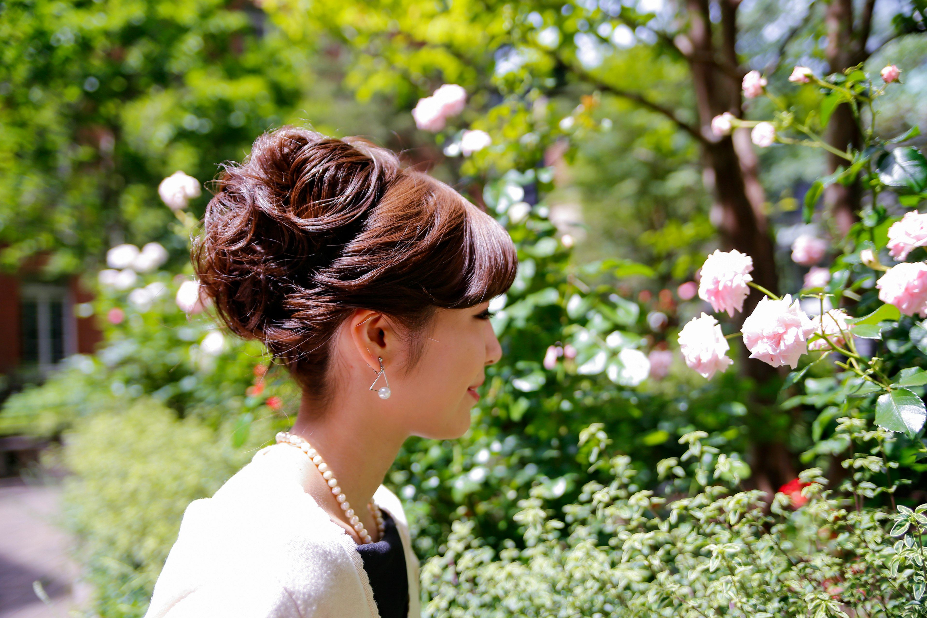 Eine Frau mit einer eleganten Frisur steht vor rosa Rosen in einem grünen Park