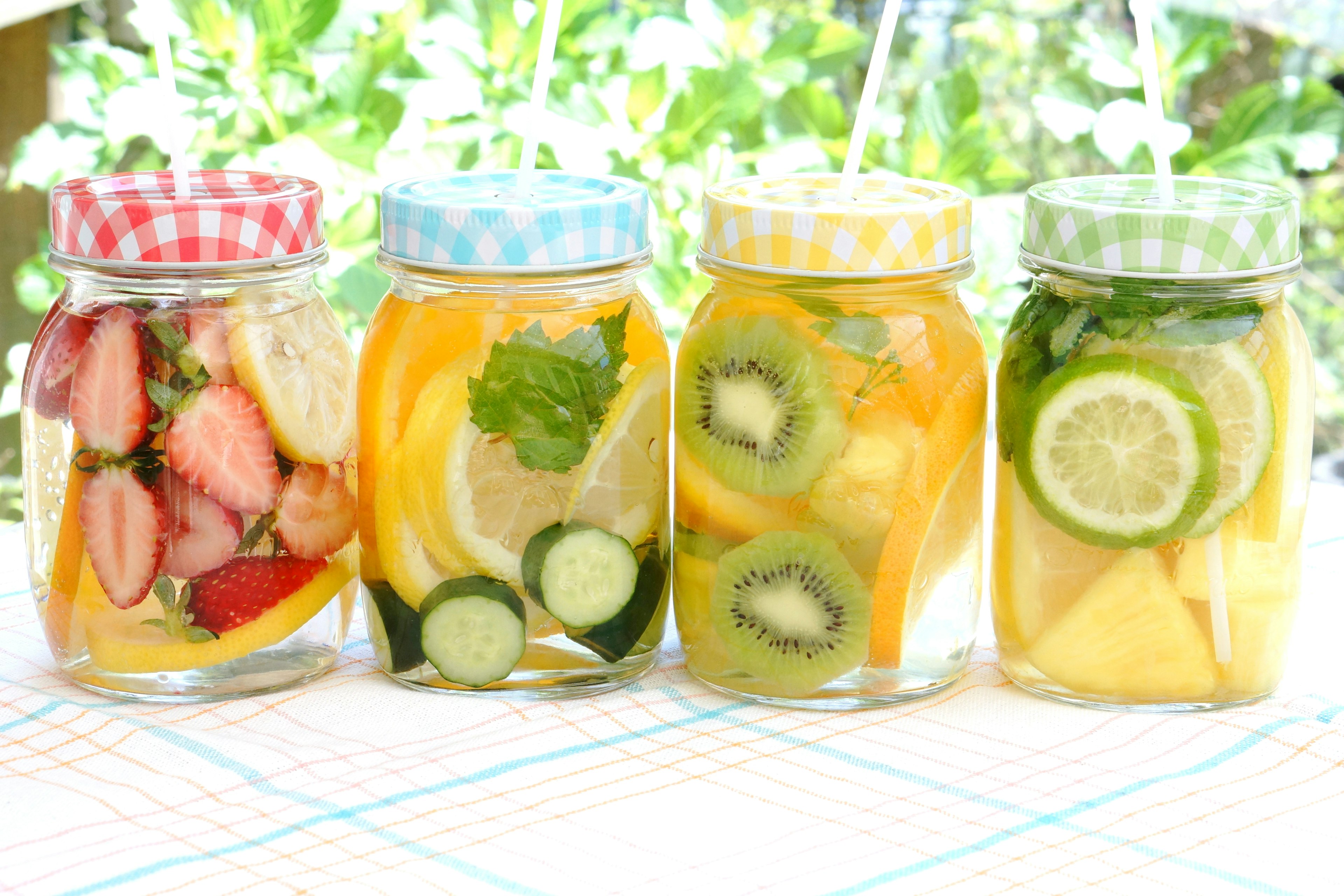 Jars of fruit and herb infused water lined up outdoors